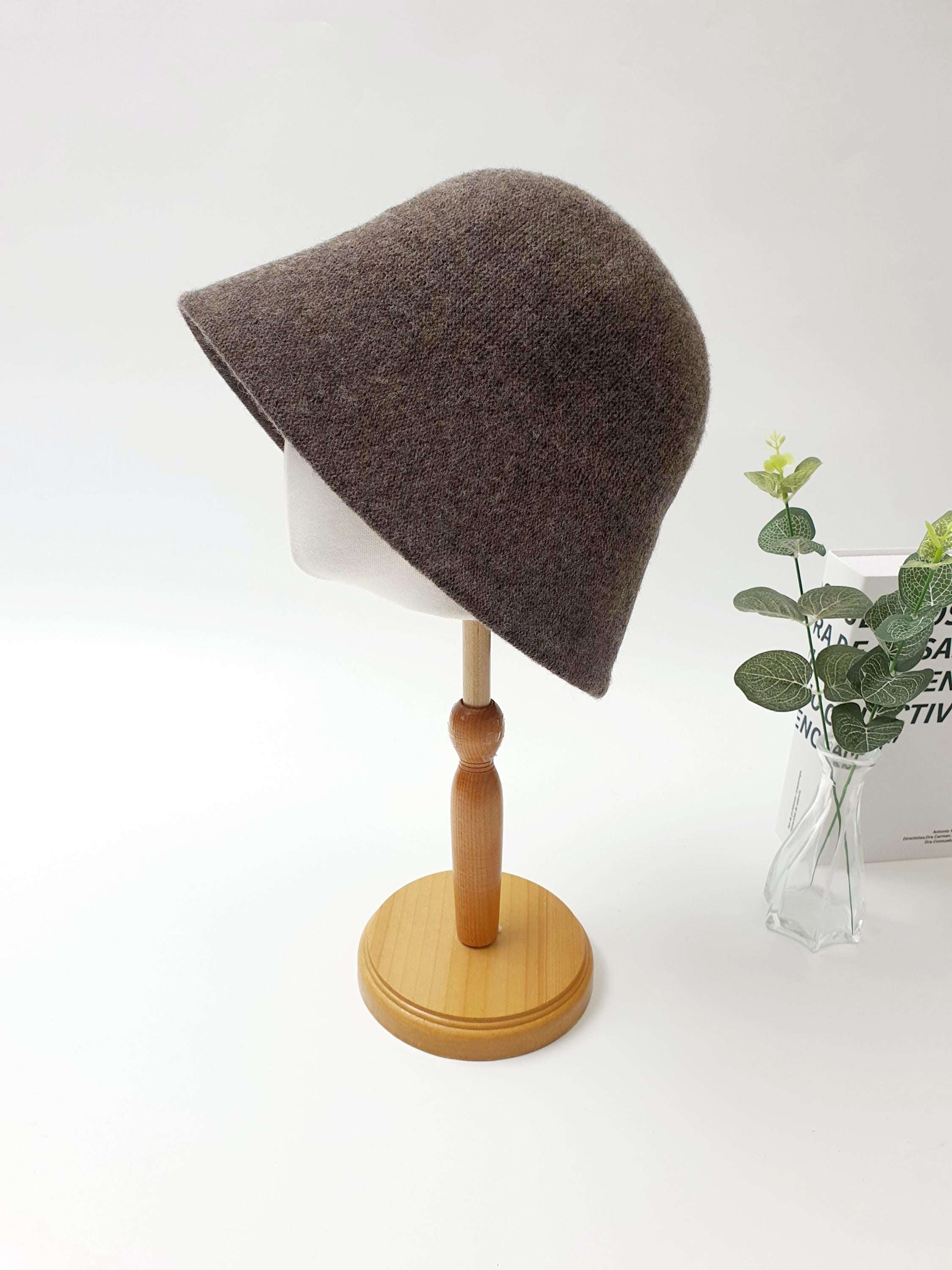 Brown bucket hat from FALL'IN WINTER, displayed on a mannequin head with a wooden stand, soft texture and a gentle sloping brim.