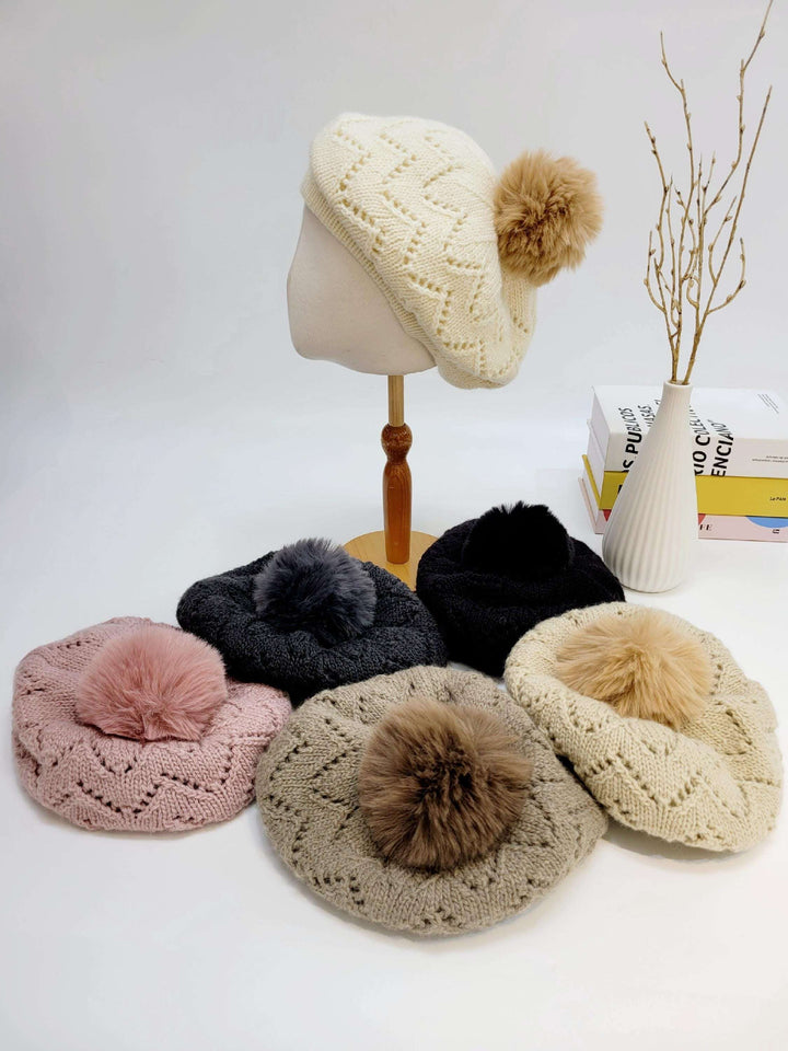 emma in paris knitted berets: Cream beret on stand, surrounded by pink, gray, taupe, black, and cream berets, each with a fluffy pom-pom