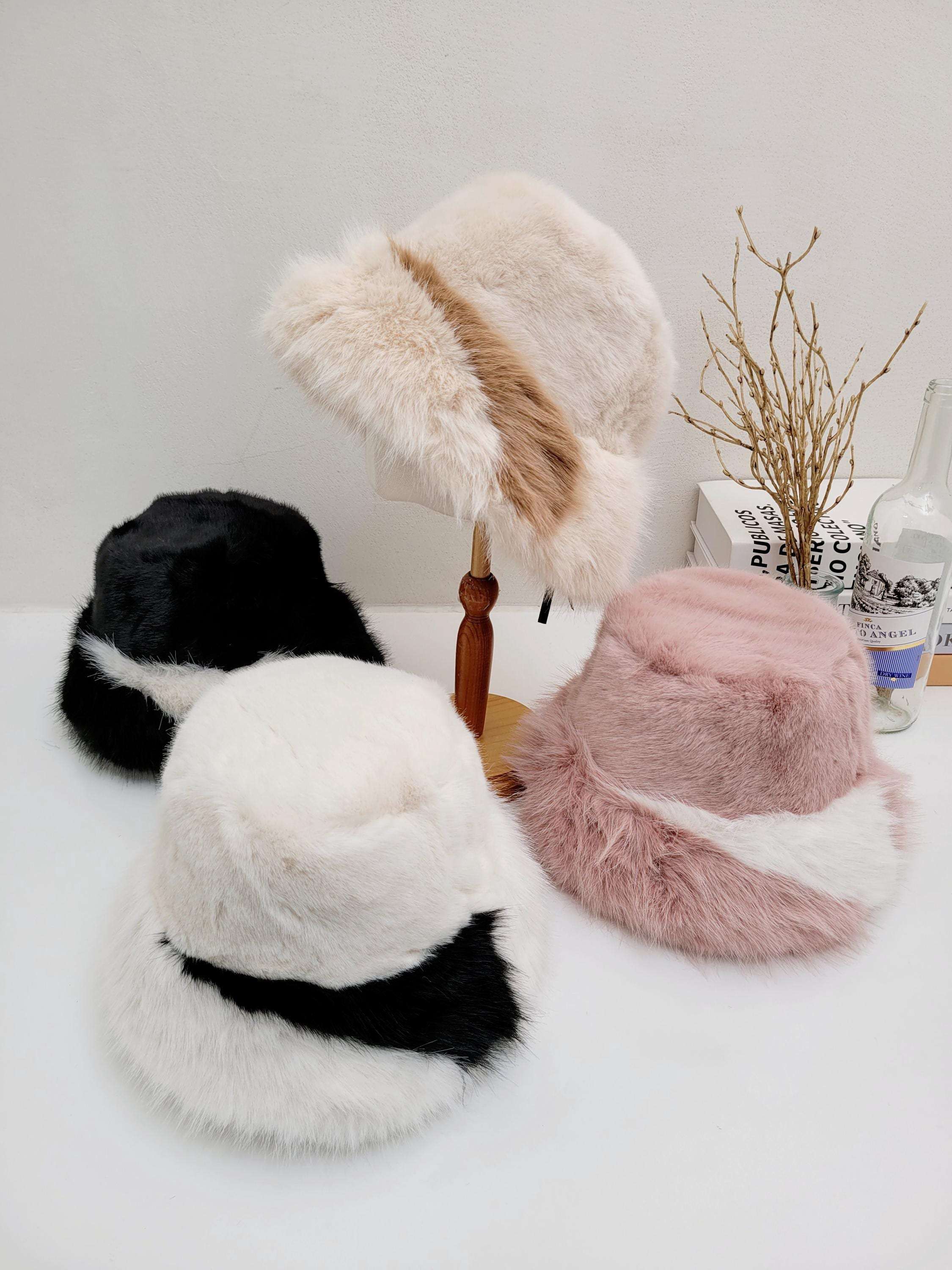 Four fluffy vegan fur hats: beige/brown, black/white, white/black, and pink/white. One beige hat is on a wooden stand.