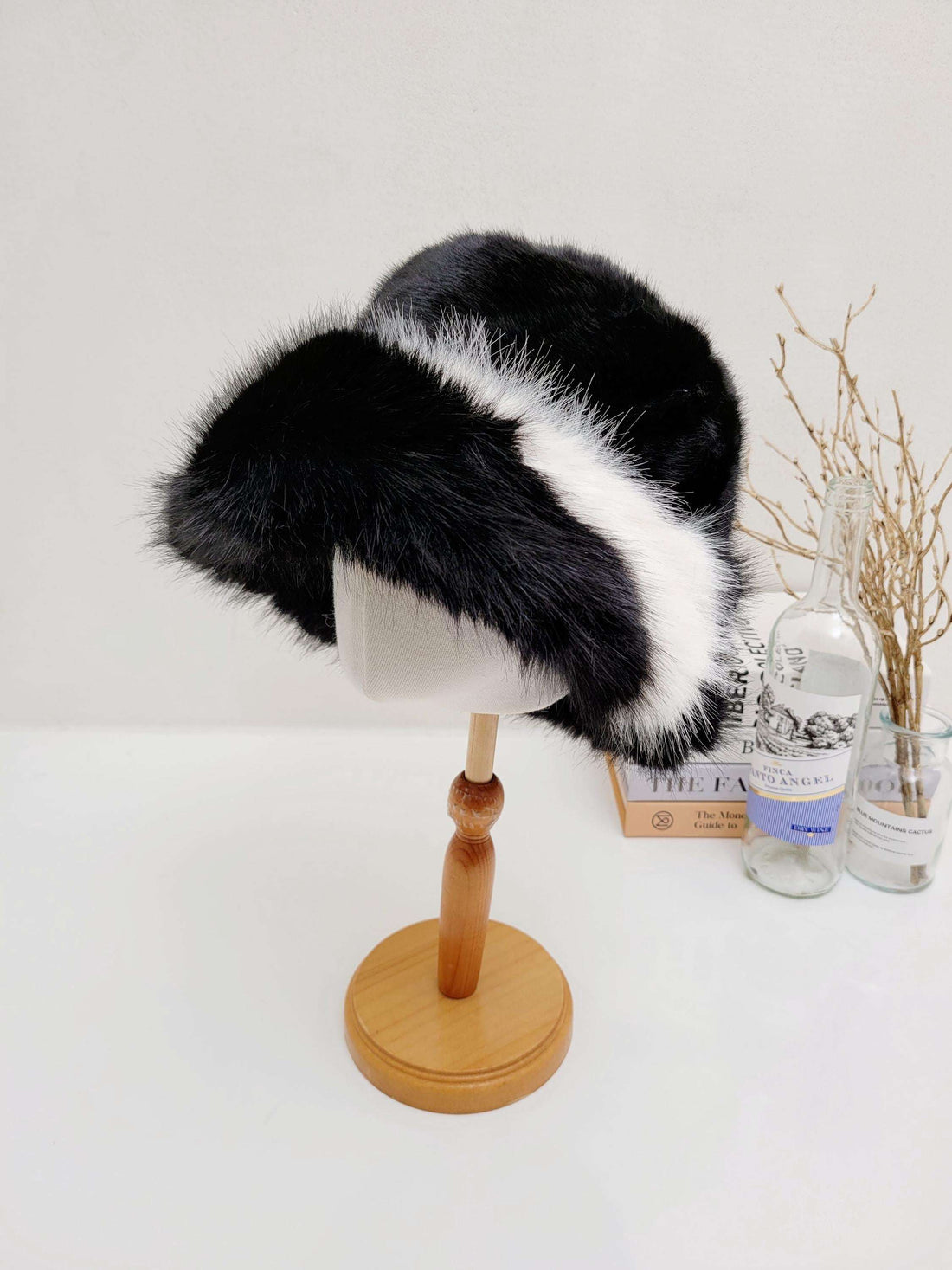 fluffy vegan fur hat in black and white, displayed on a wooden stand. A stylish and cruelty-free headwear option.