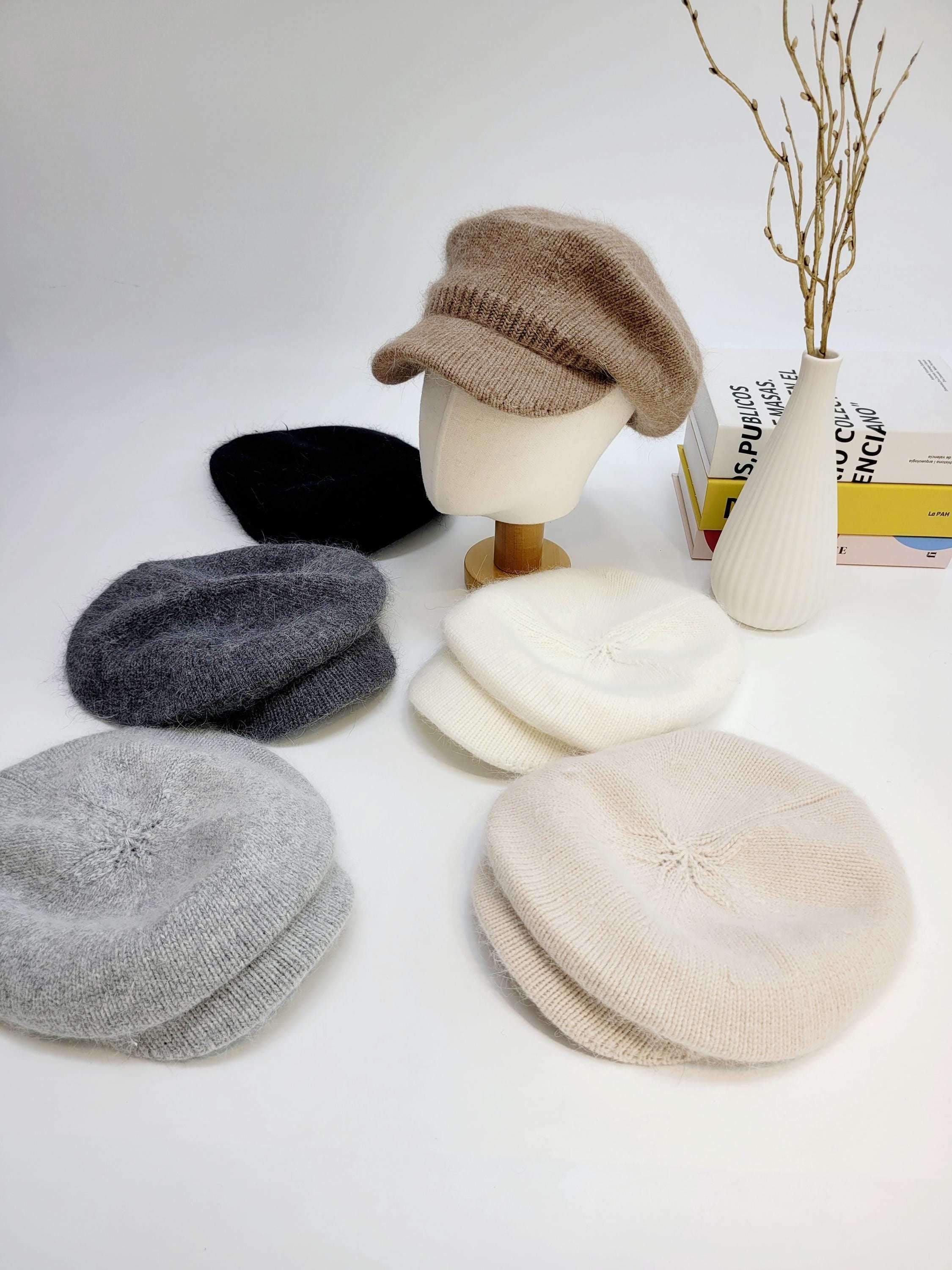 ANGELINA IN LOVE knit berets in beige, white, light gray, dark gray, and black. Soft, cozy hats arranged on a white surface, one styled on a mannequin head.
