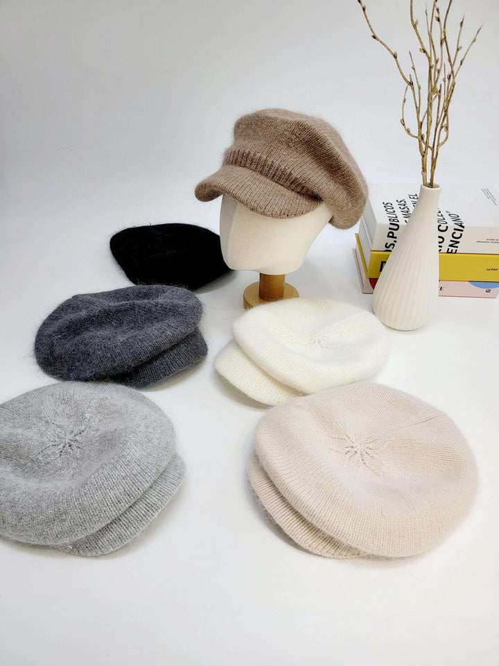 ANGELINA IN LOVE knit berets in beige, white, light gray, dark gray, and black. Soft, cozy hats arranged on a white surface, one styled on a mannequin head.
