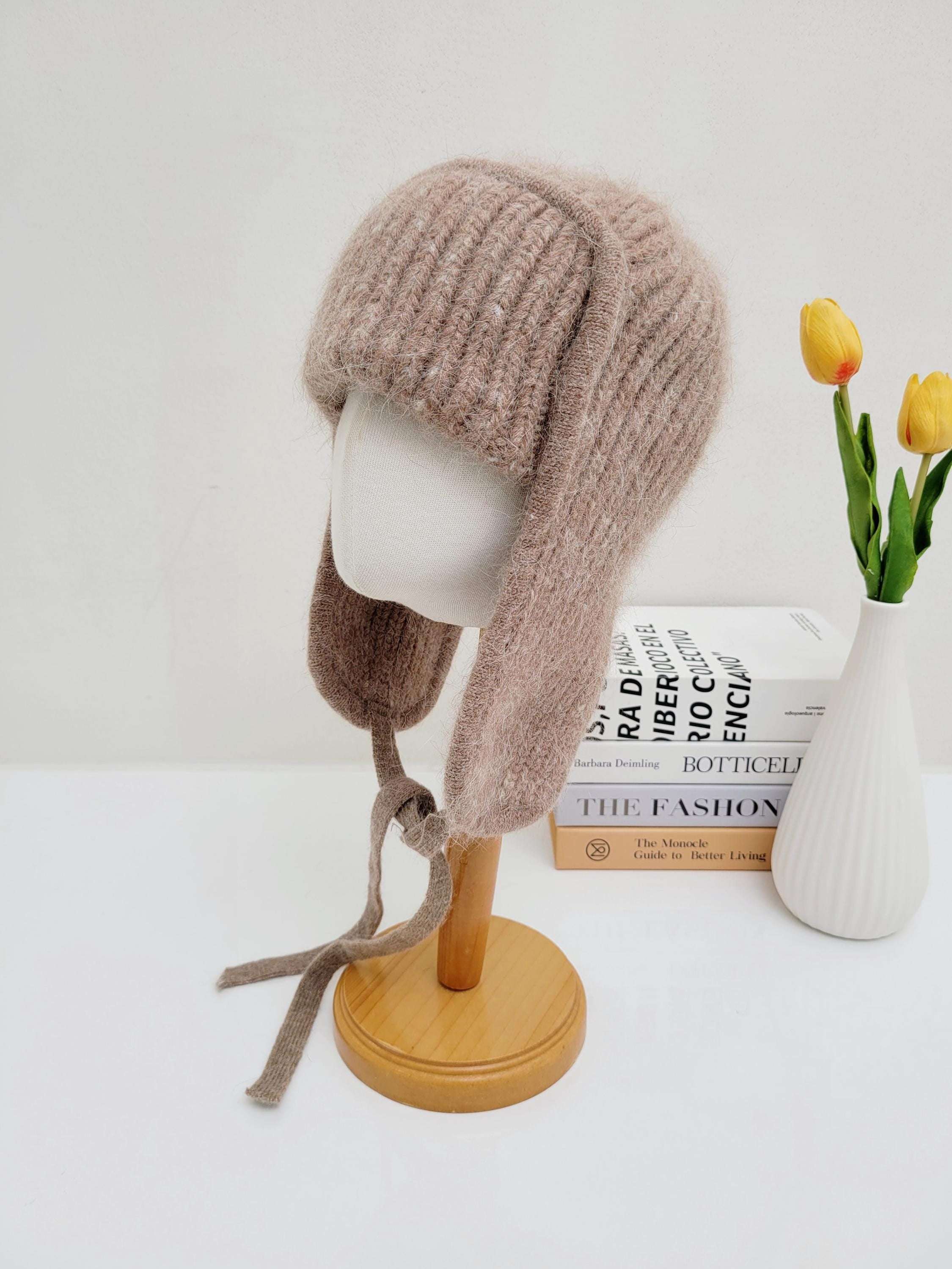 beige knitted west mountain angora trapper hat on a mannequin head, featuring ear flaps with ties for a secure fit.