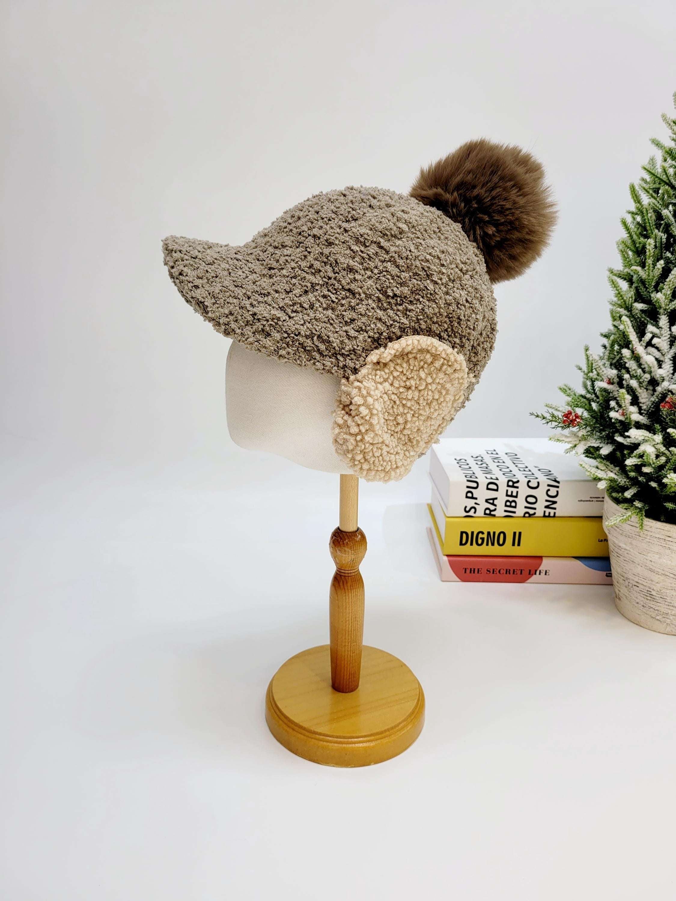 WOOF WOOF: Brown knit hat with cozy ear flaps and a fluffy pompom, displayed on a mannequin head.