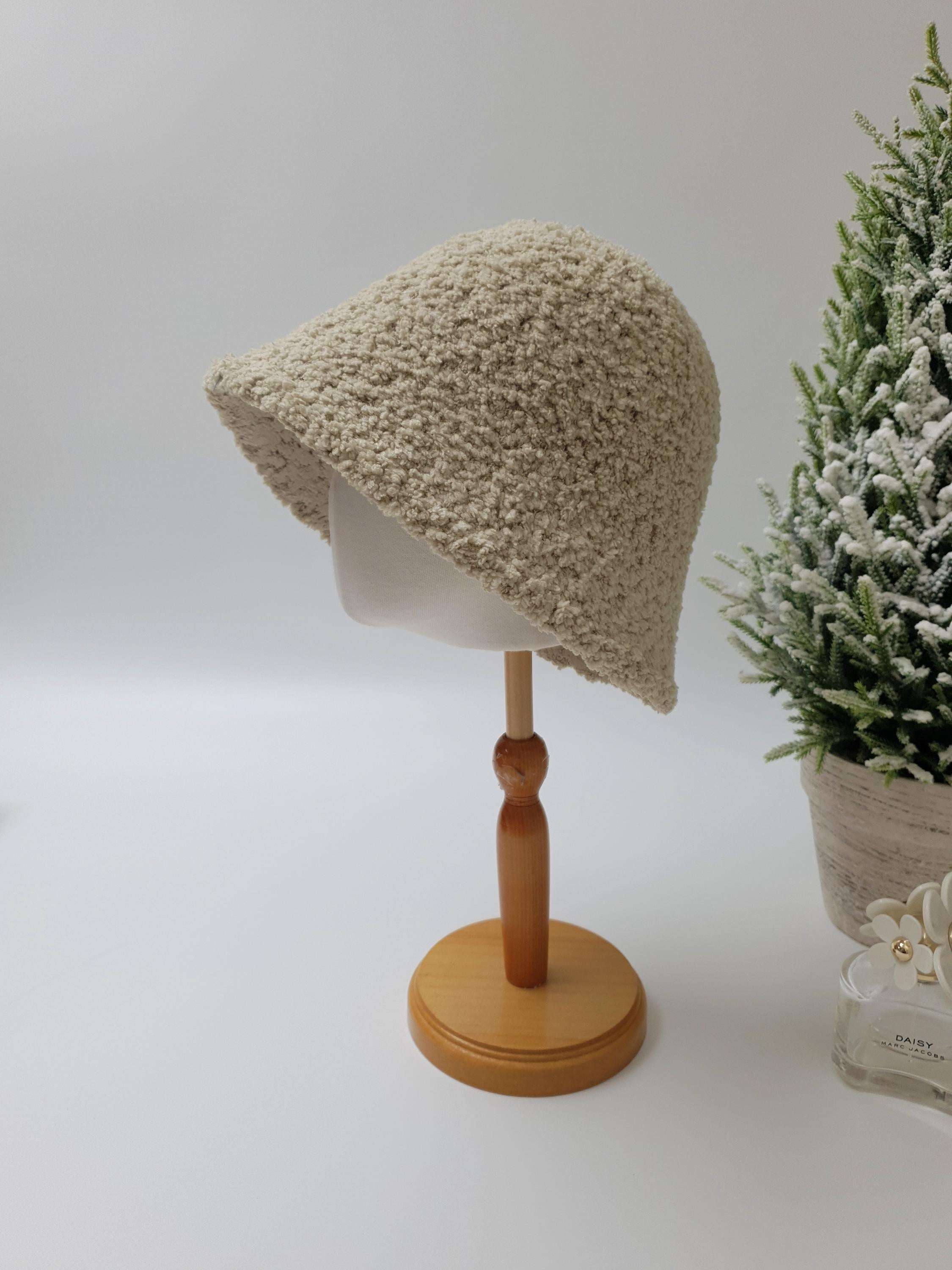 Beige sherpa bucket hat on a wooden display stand. Cozy and stylish, perfect for any outfit.