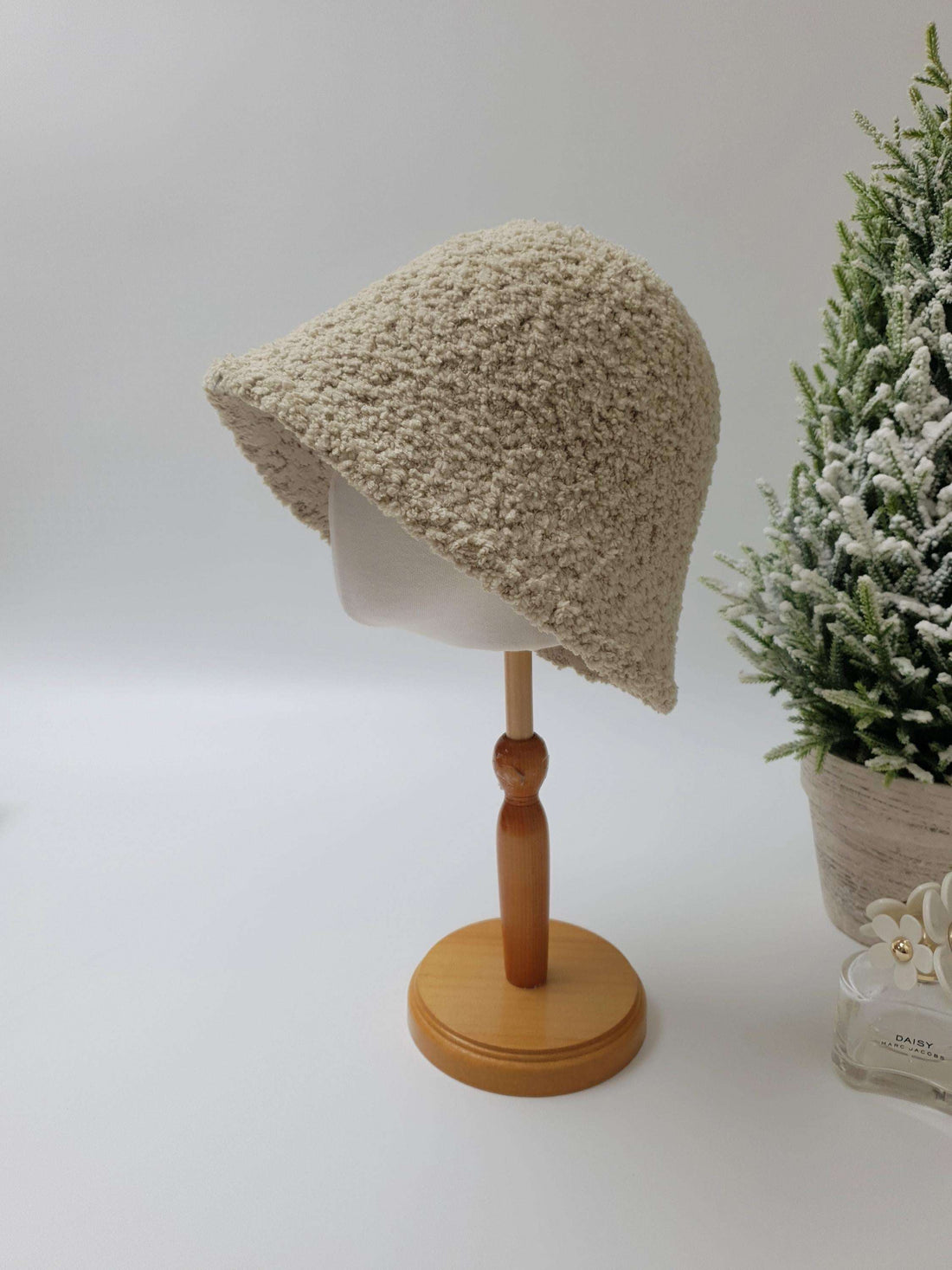 Beige sherpa bucket hat on a wooden display stand. Cozy and stylish, perfect for any outfit.