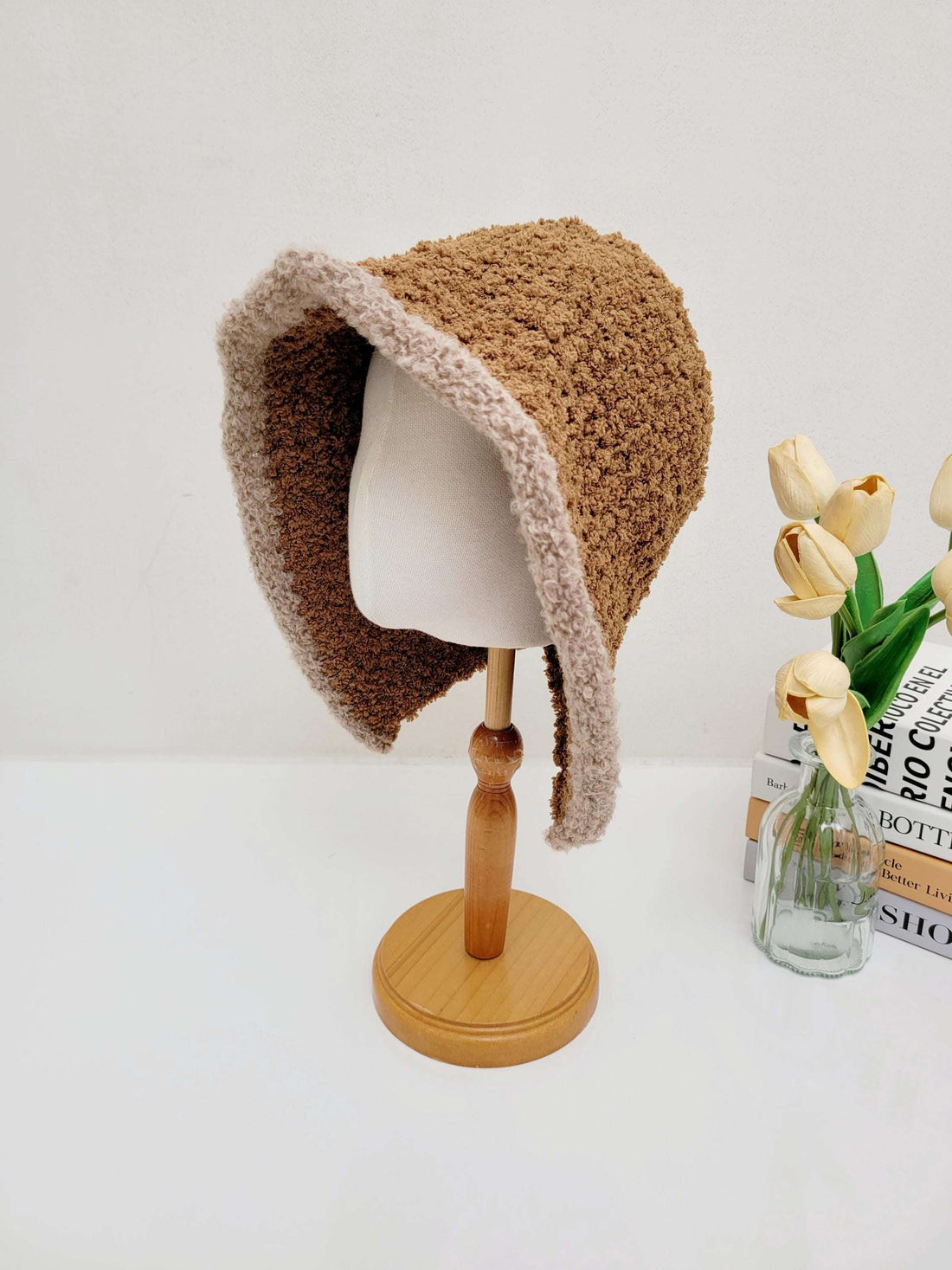 Brown wool hooded hat with a soft tan trim, displayed on a wooden stand. Perfect for warmth and style.