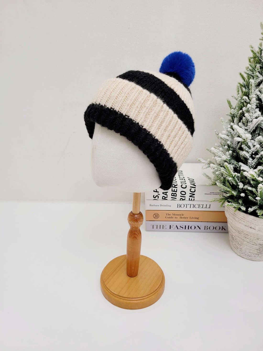 PARIS - B&W beanie: A beige knit winter hat with bold black stripes and a playful blue pompom, displayed on a mannequin head.