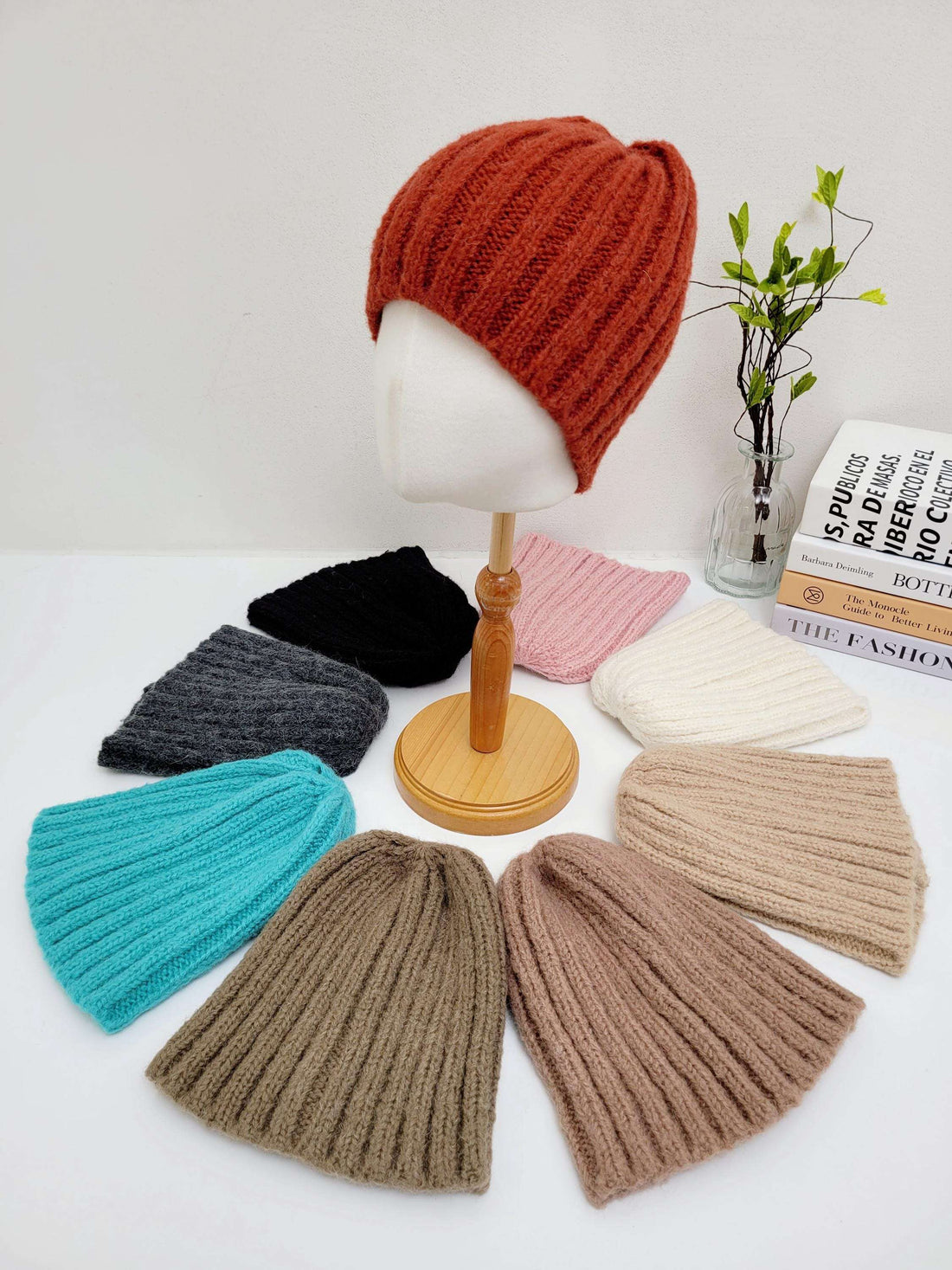 WIDE RIB WOOL BEANIE: Assorted color knitted beanies (orange, black, pink, white, gray, teal, brown) arranged around a mannequin head