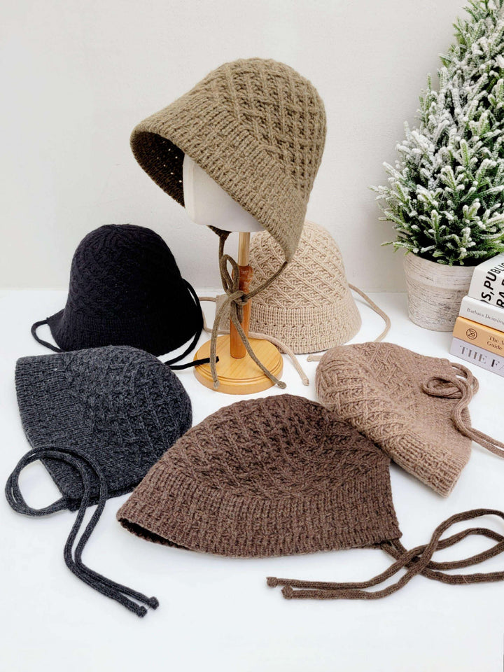Assorted knitted wool bucket hats in neutral shades: brown, beige, gray, and black. One hat is displayed on a mannequin head stand.
