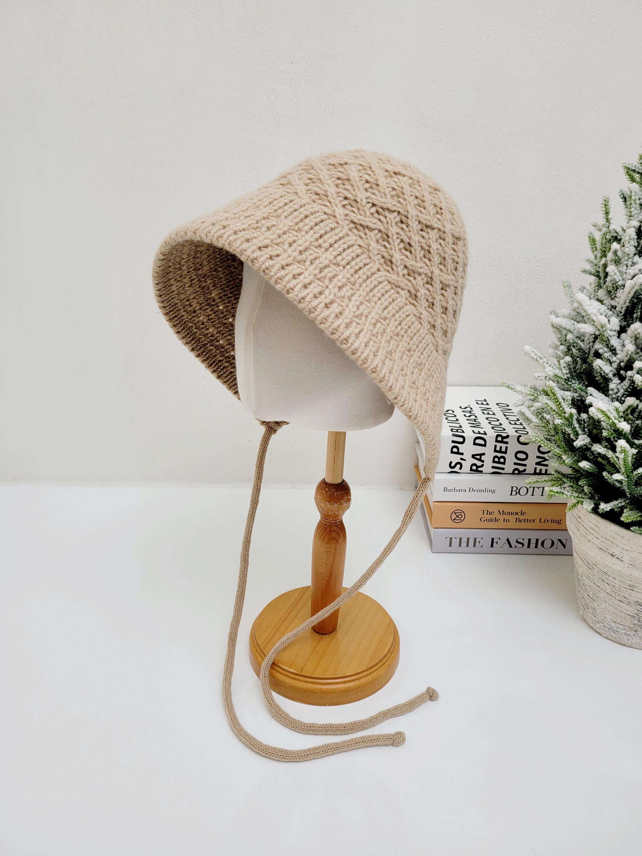 Beige knitted wool bucket hat with chin ties, displayed on a mannequin head.