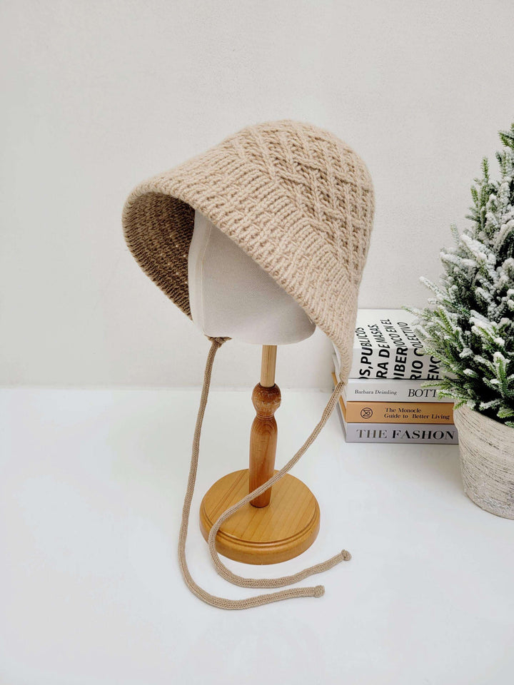 Beige knitted wool bucket hat with chin ties, displayed on a mannequin head.