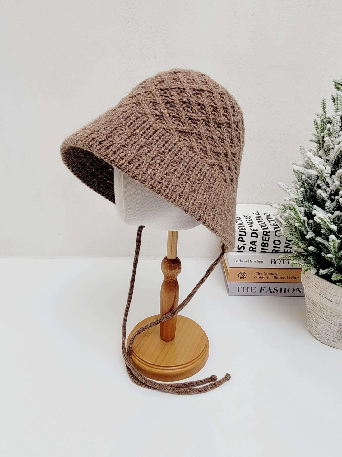 Brown knitted wool bucket hat with chin ties, displayed on a mannequin head. The hat features a textured knit pattern and soft, floppy brim.