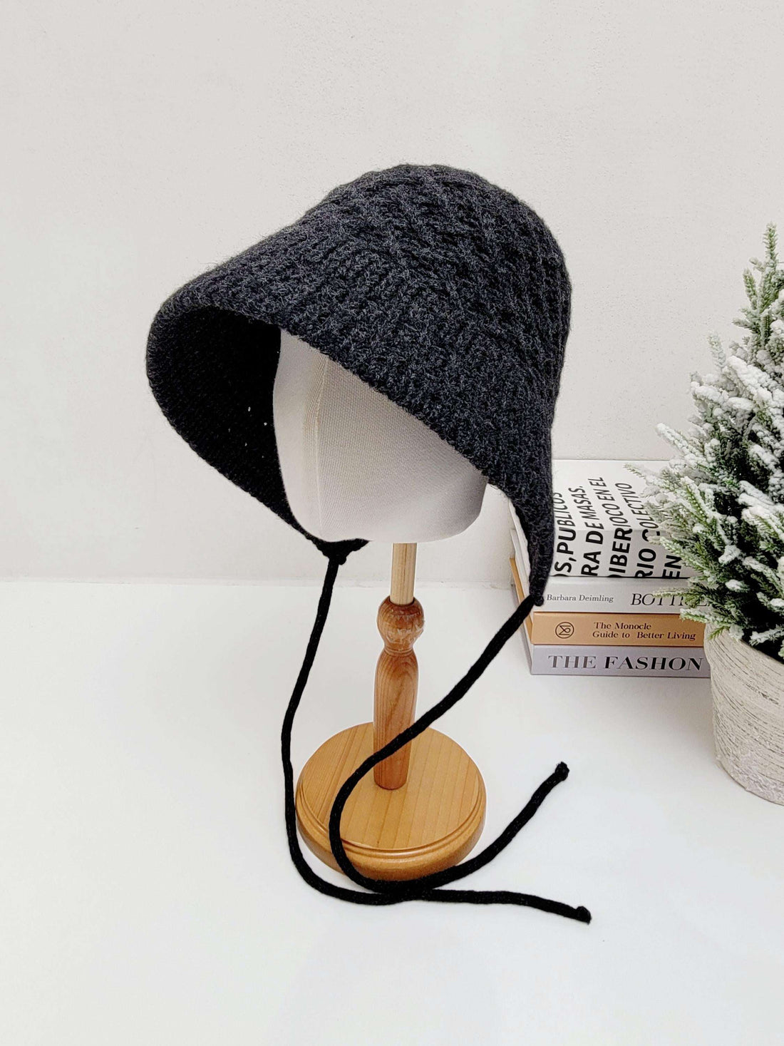 Gray knitted wool bucket hat with tie strings, displayed on a wooden stand. Cozy and stylish headwear.