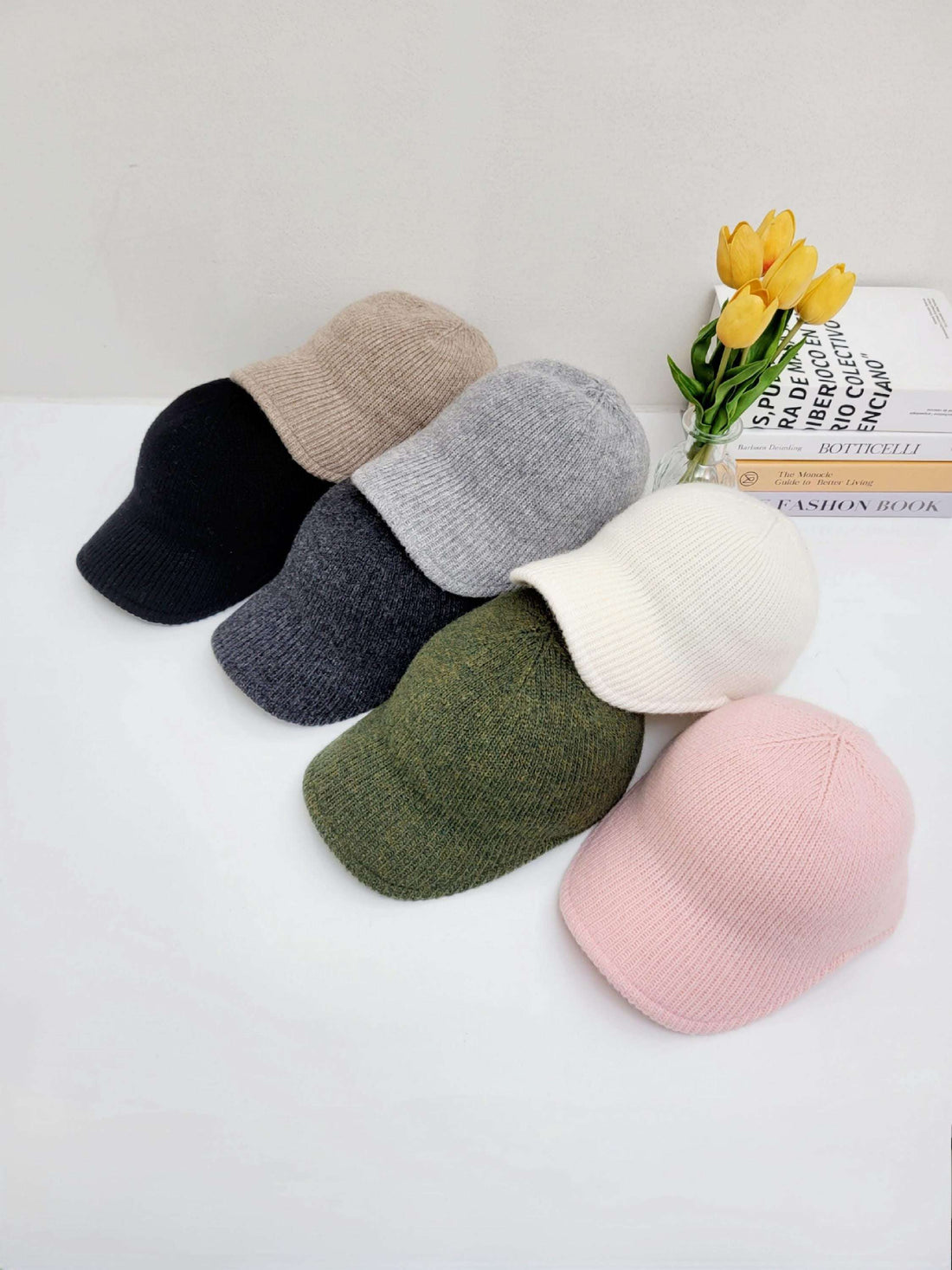 Six ribbed cap hats in black, beige, grey, olive green, white, and pink. Knit caps stacked on a white surface.