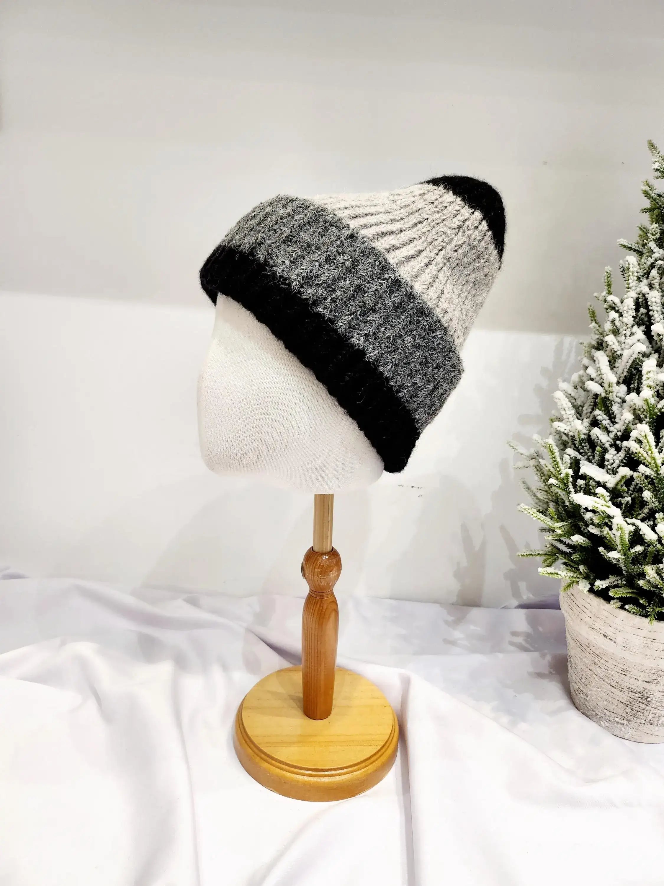 anna angora beanie: a cozy, striped wool hat in black, grey, and off-white, displayed on a mannequin head.