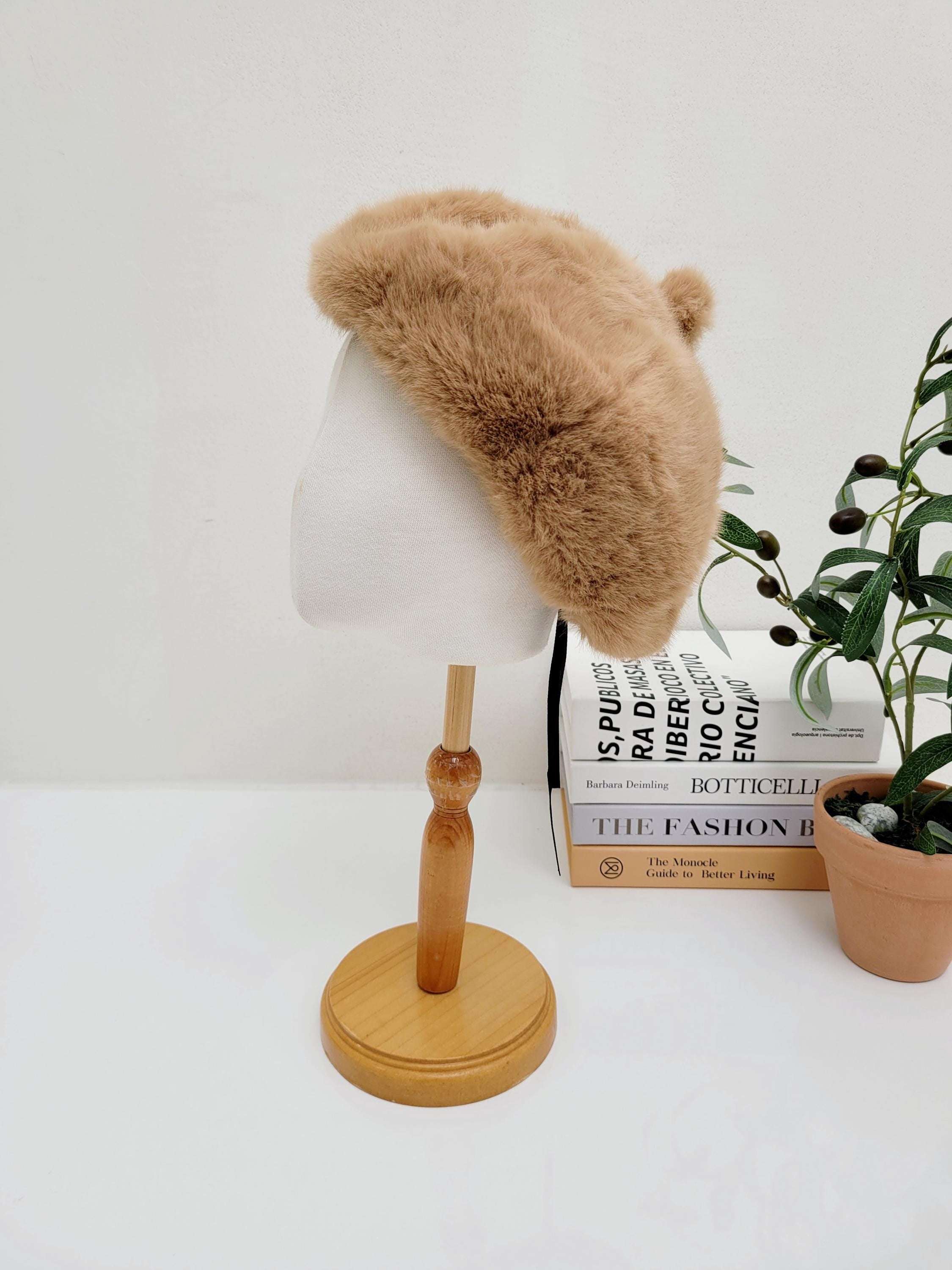 Light brown faux fur paris in winter beret with cute pom-poms, displayed on a mannequin head for stylish cold-weather fashion.