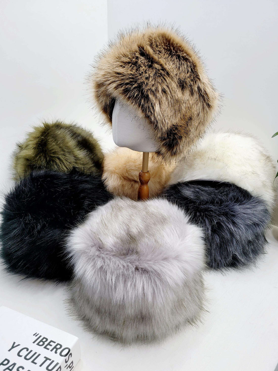 Assorted fluffy hats, including the sonya hat fluffy, in brown, green, black, gray, and white, displayed on a white surface.