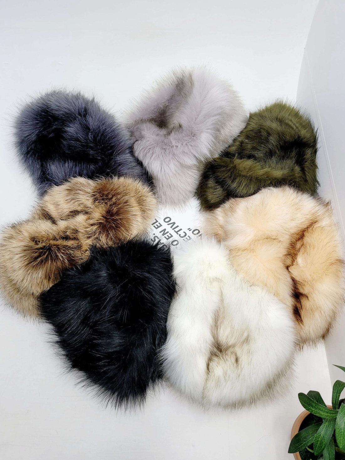 SONYA HAT FLUFFY: Assortment of fluffy fur pieces in black, white, gray, brown, olive green, and cream, arranged in a circle.