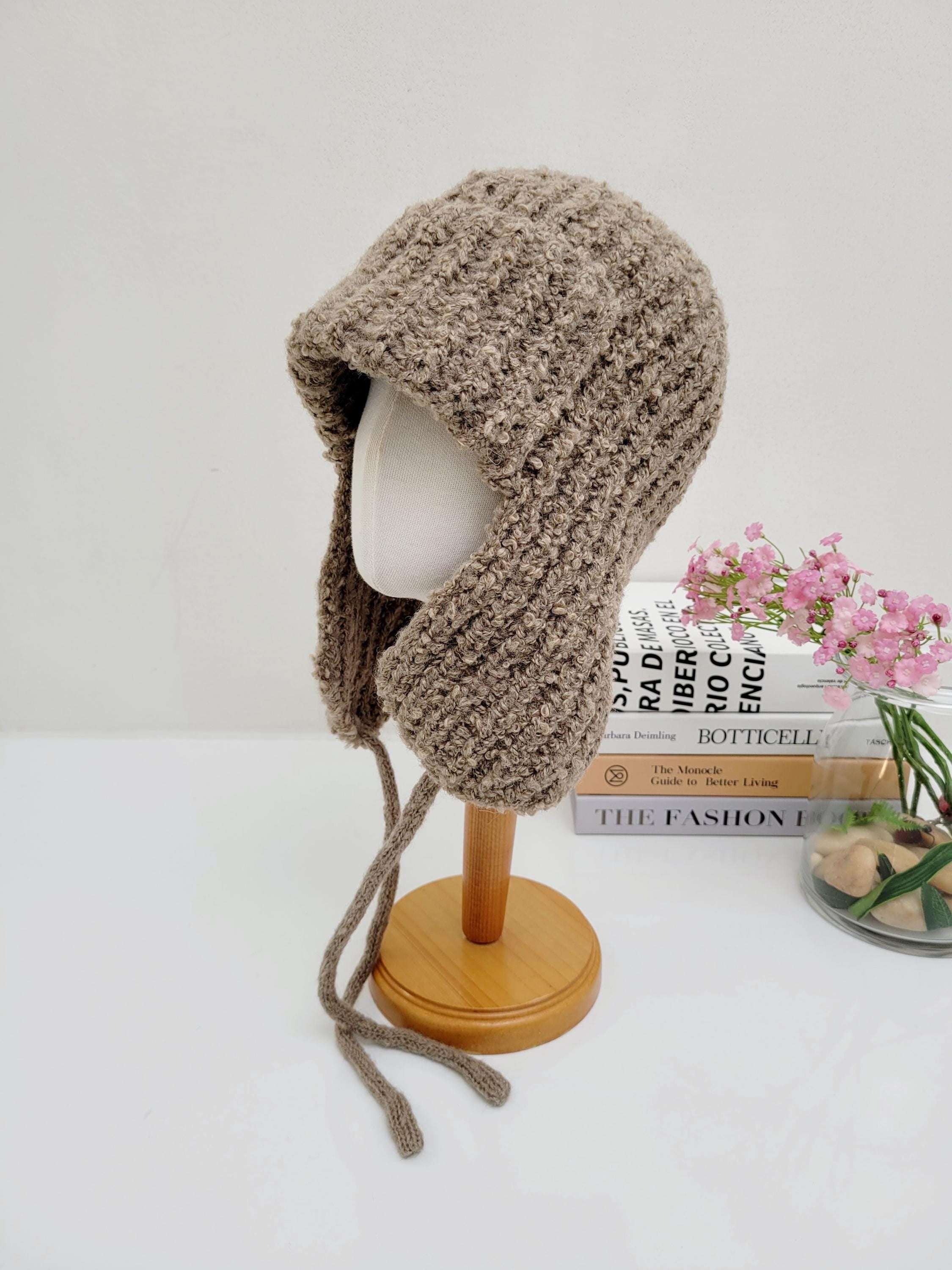 Brown knitted wool earflap hat with tie strings, displayed on a mannequin. Cozy & stylish headwear for cold weather.