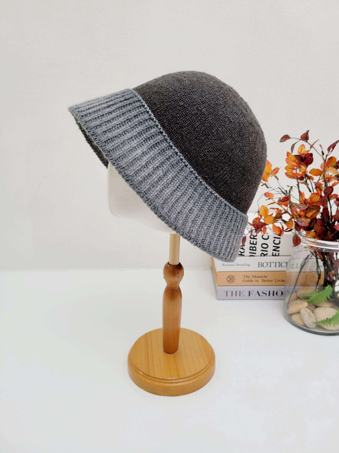Dark gray knitted diana hat with a ribbed light gray brim, displayed on a wooden stand.