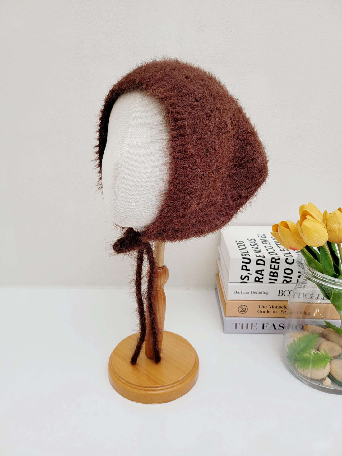 Brown fuzzy little riding hood bonnet on a mannequin head, featuring soft textured material and tie closure.