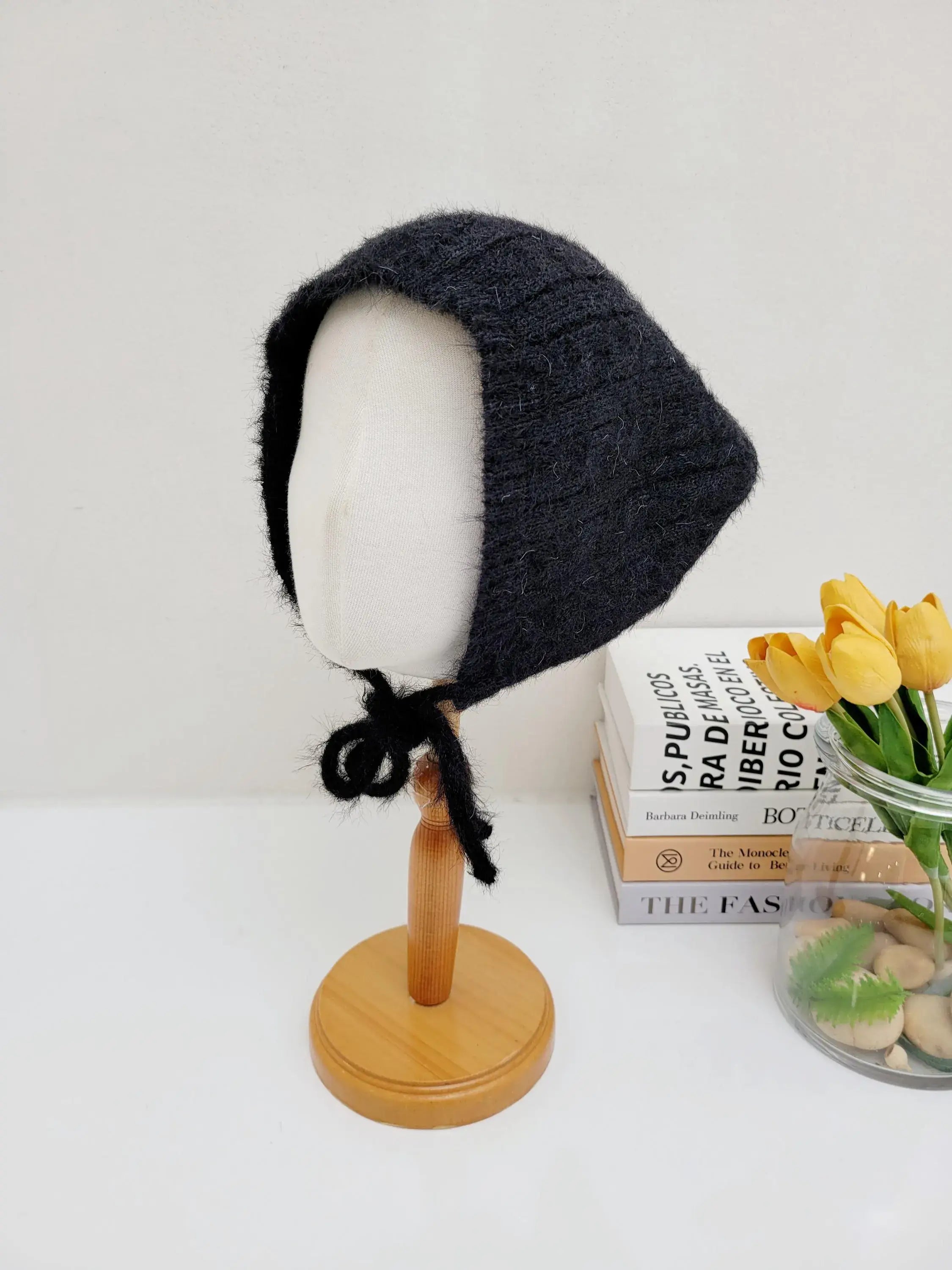 Black knitted little riding hood bonnet on a mannequin, featuring soft yarn and tie closure.
