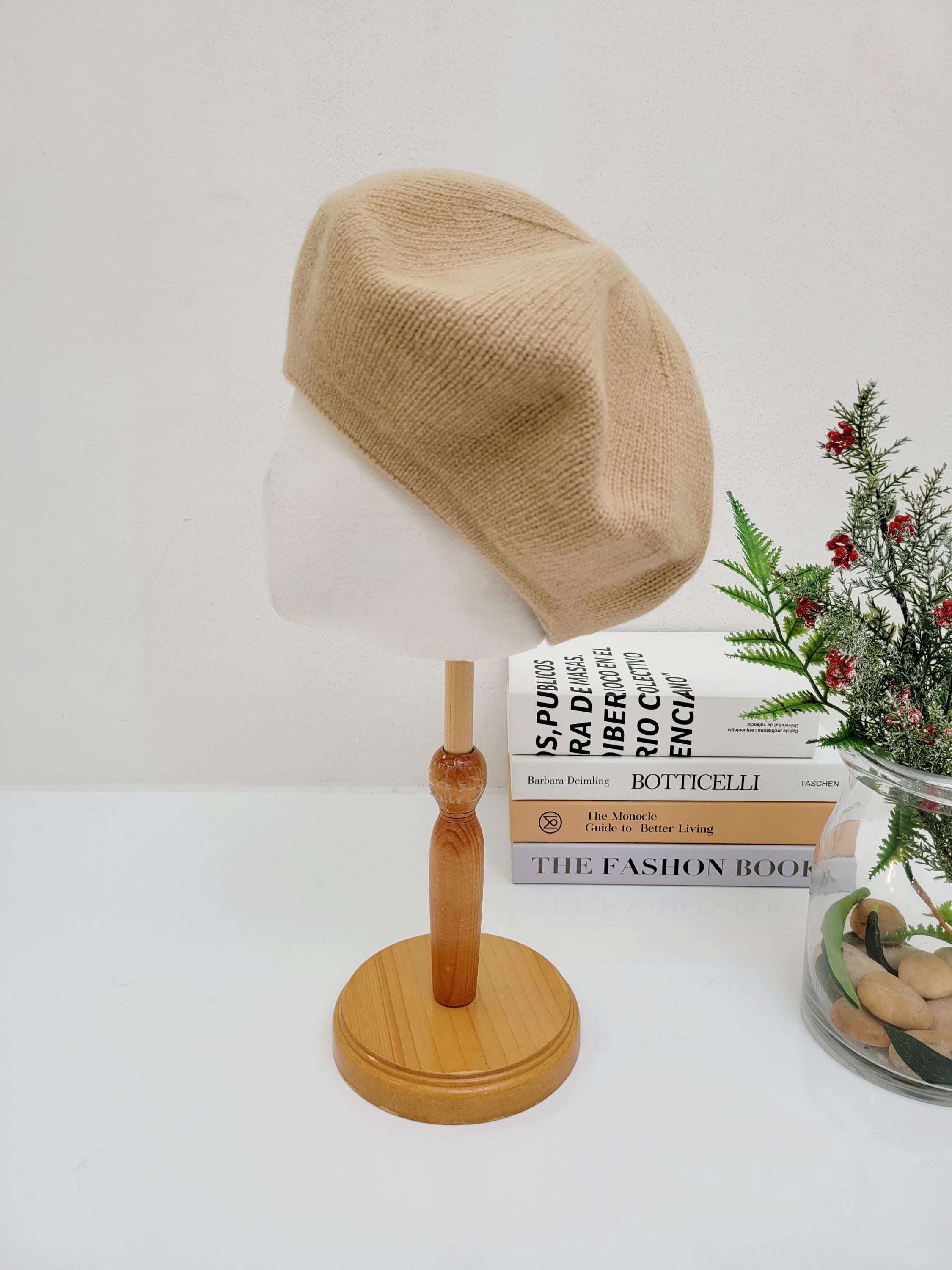 paris wool beret in soft beige, displayed on a wooden stand. A stylish and classic accessory.