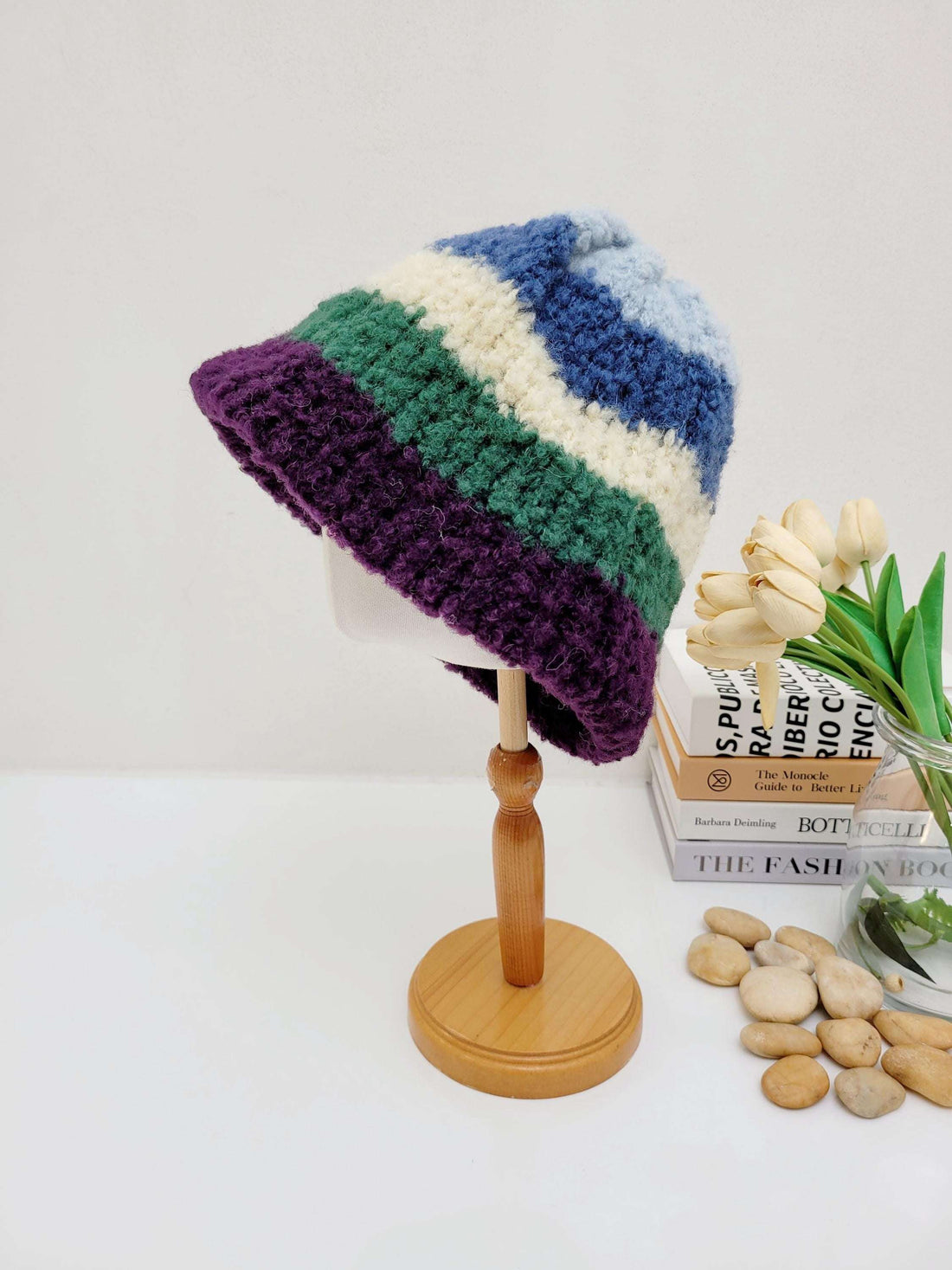 Striped tokyo beanie: chunky knit hat with purple, green, cream, and blue bands, displayed on a wooden stand.