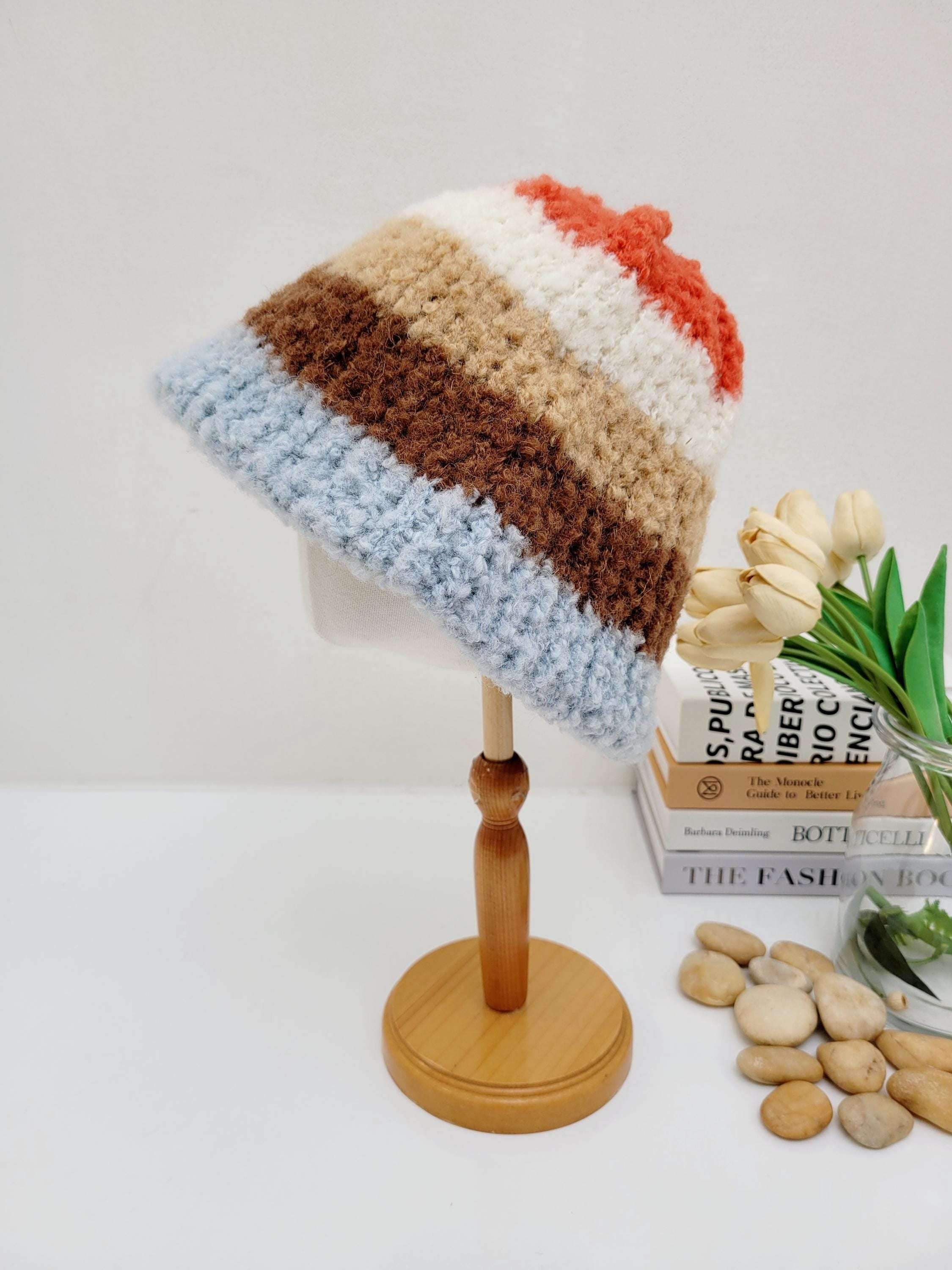 Striped tokyo beanie in blue, brown, tan, white, and orange knit, displayed on a wooden stand. A cozy and stylish winter accessory.