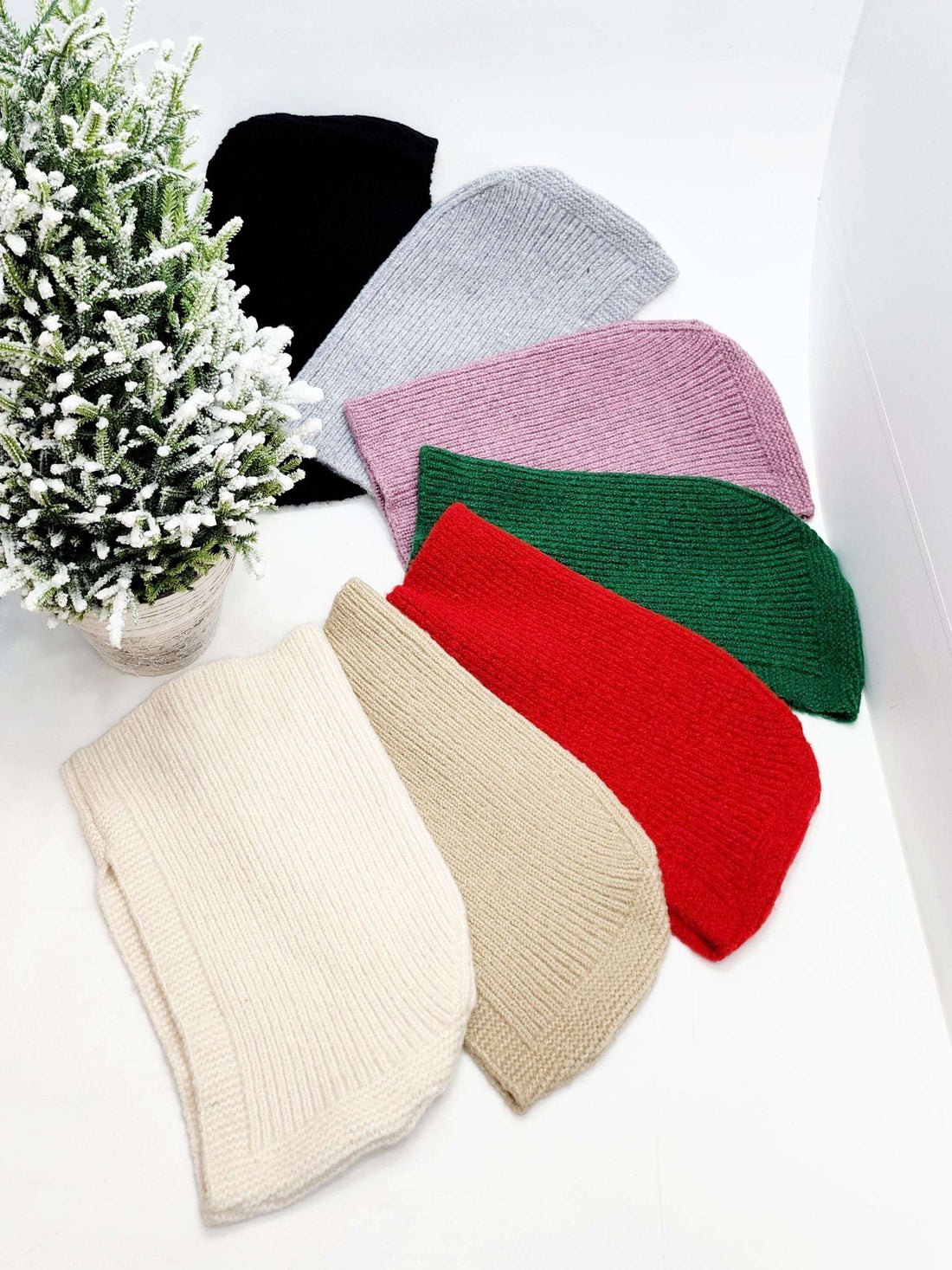 Assorted colorful knitted balaclavas by Little Riding Hood displayed with a snowy potted plant