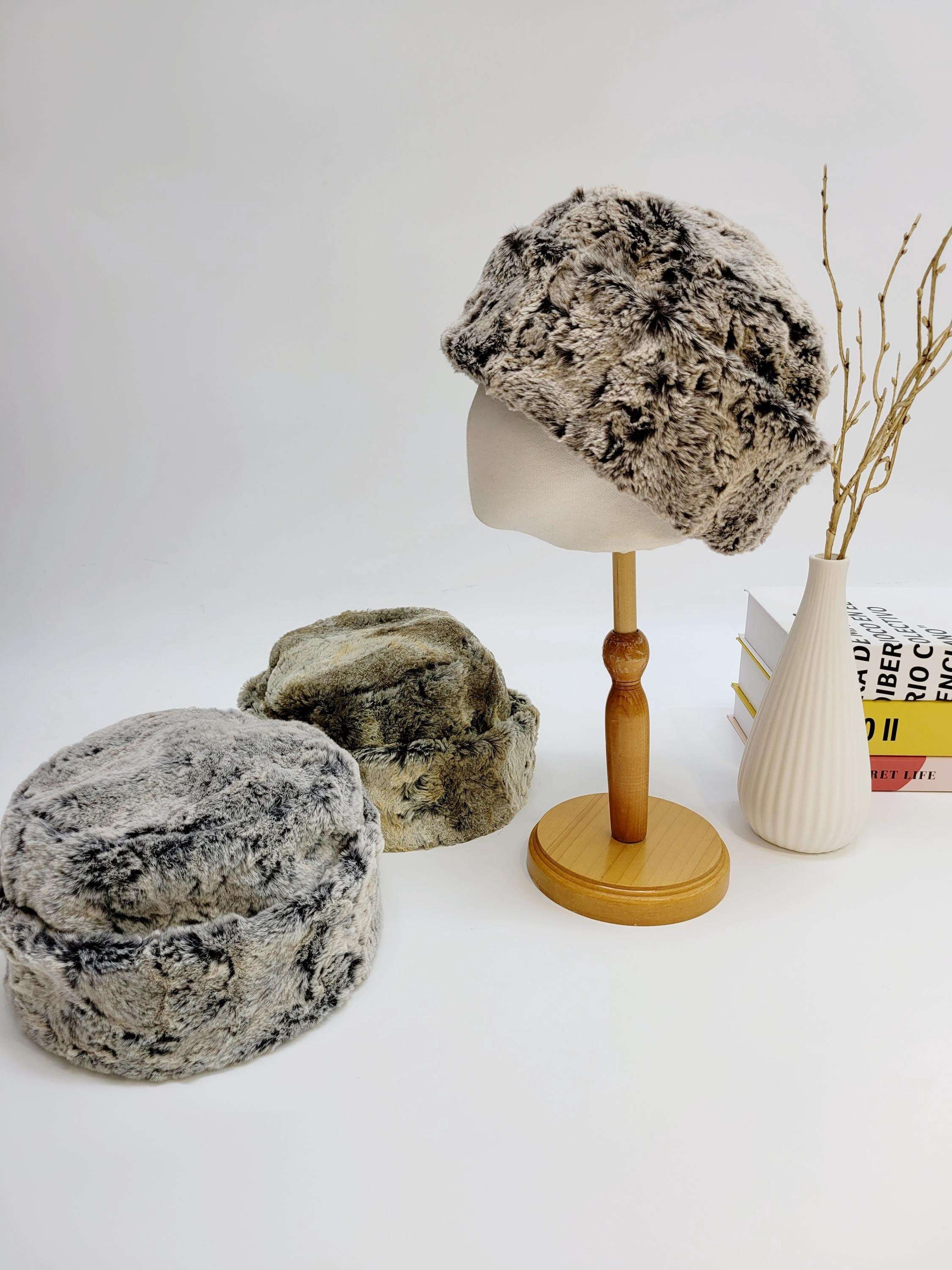 Three gray faux fur beanies displayed on mannequin heads, with a wooden stand holding a branch beside them.