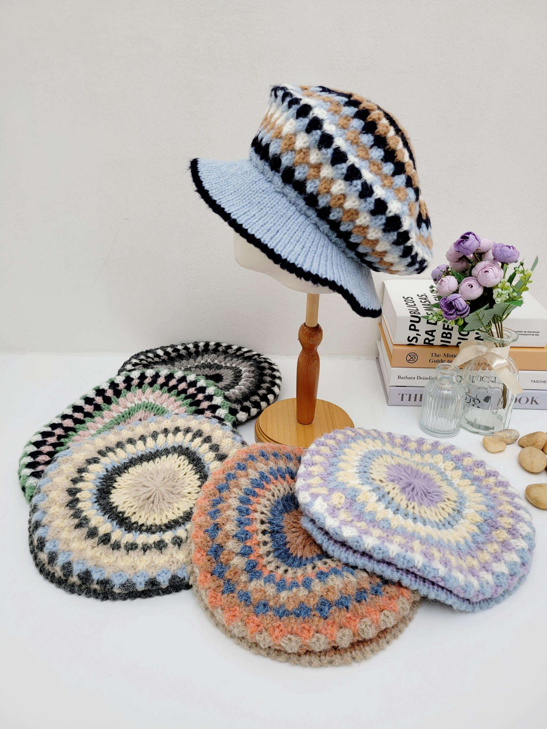 A collection of crocheted beret hats in various colors displayed on a wooden stand and table.