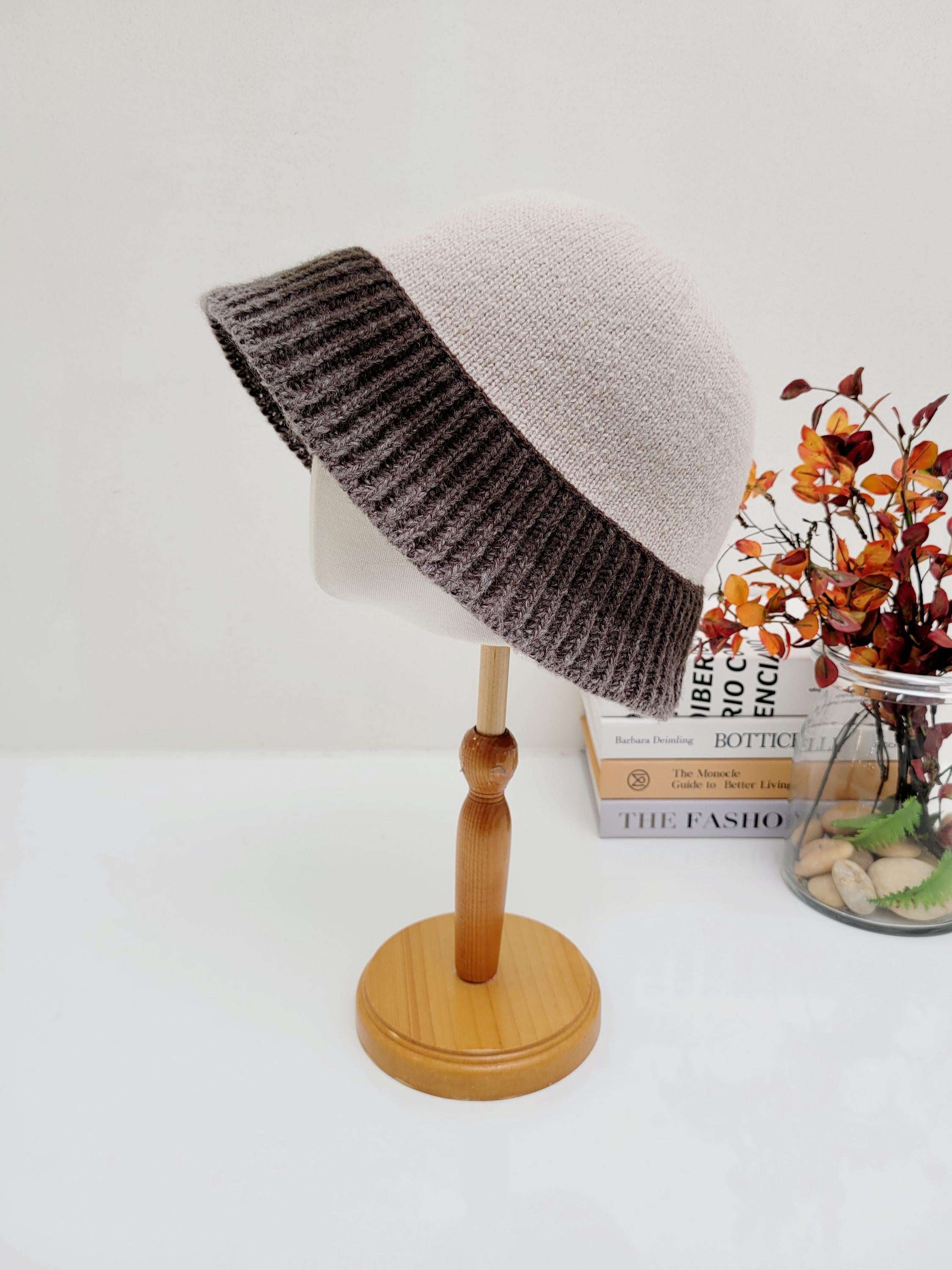 diana hat: Beige knitted hat with a wide, dark brown brim, displayed on a wooden stand.