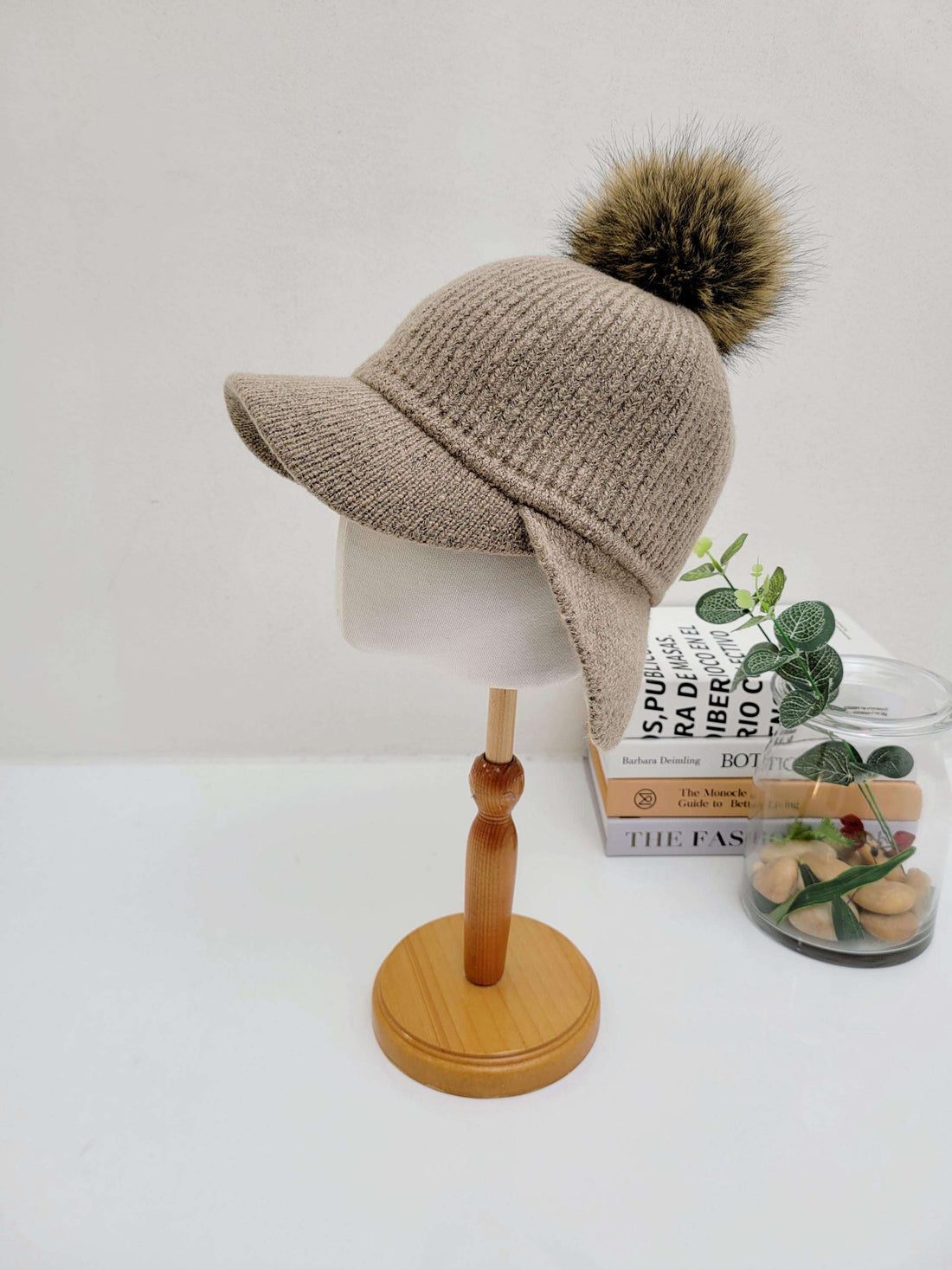 Beige ribbed cap - pom, a knit hat with a brim and a fluffy brown faux fur pompom, displayed on a mannequin head.