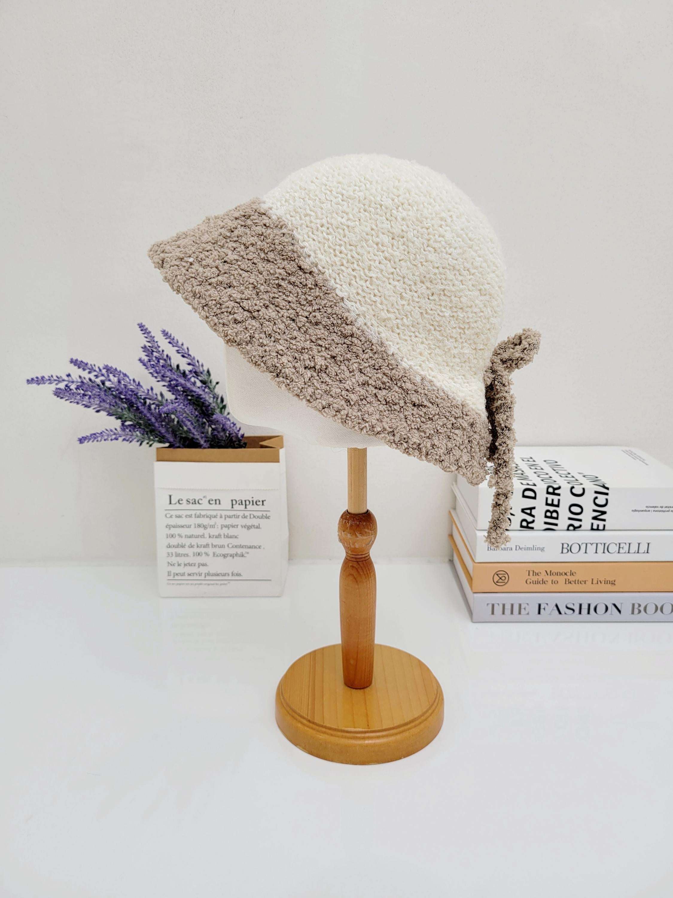 BOHO BUCKET - SHERPA: Cream and beige crocheted bucket hat with a cozy sherpa-like texture, displayed on a wooden stand.