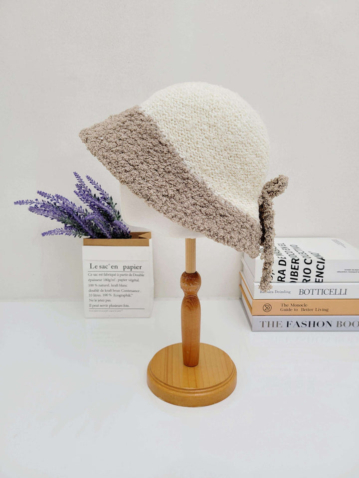 BOHO BUCKET - SHERPA: Cream and beige crocheted bucket hat with a cozy sherpa-like texture, displayed on a wooden stand.