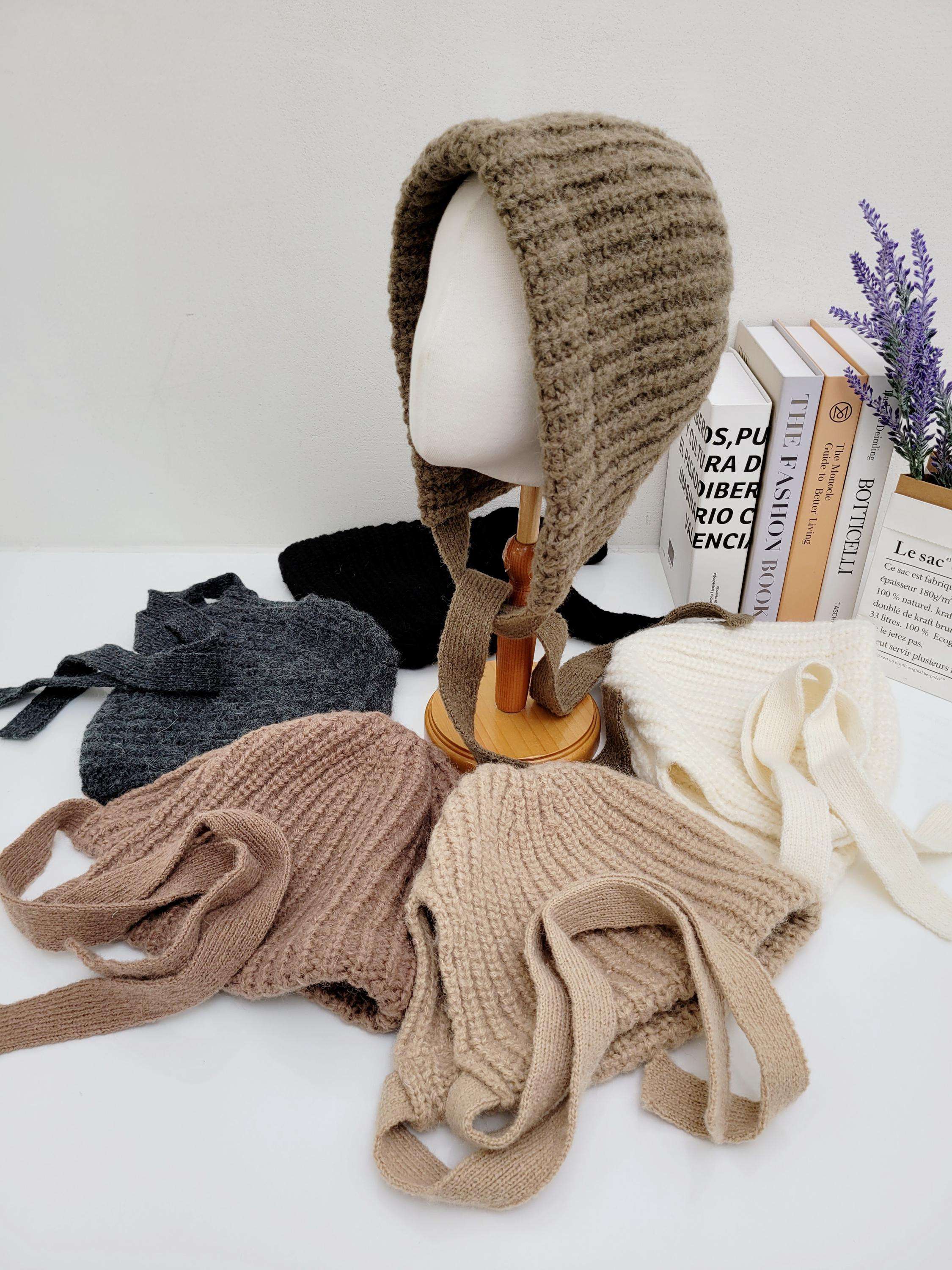 TOUR LE JOUR knitted bonnets in brown, beige, gray, black, and white, some with tie closures, displayed on a white surface and mannequin head.