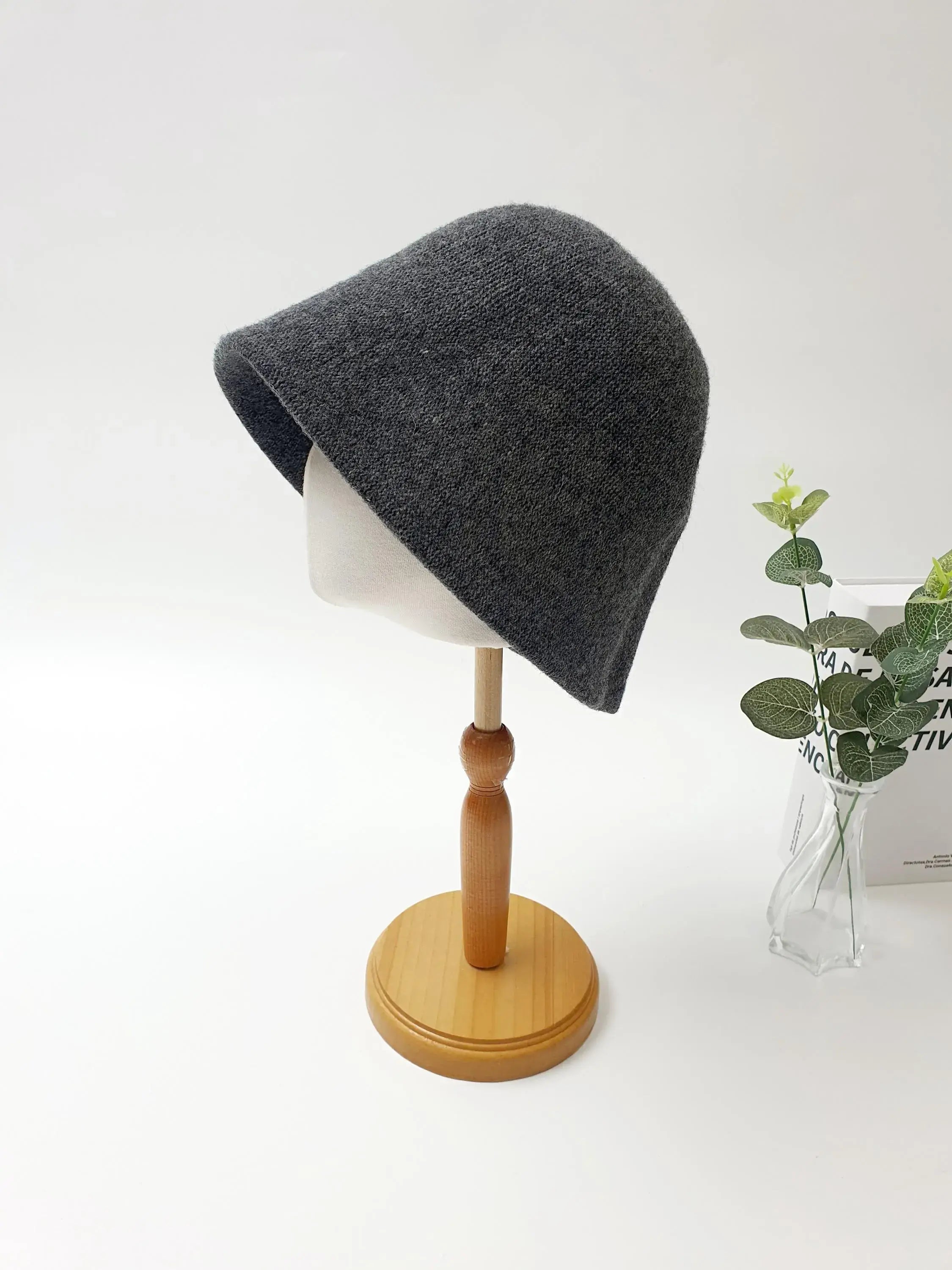 Dark gray knit bucket hat from fall'in winter, displayed on a wooden stand with greenery. Cozy and stylish for winter wear.