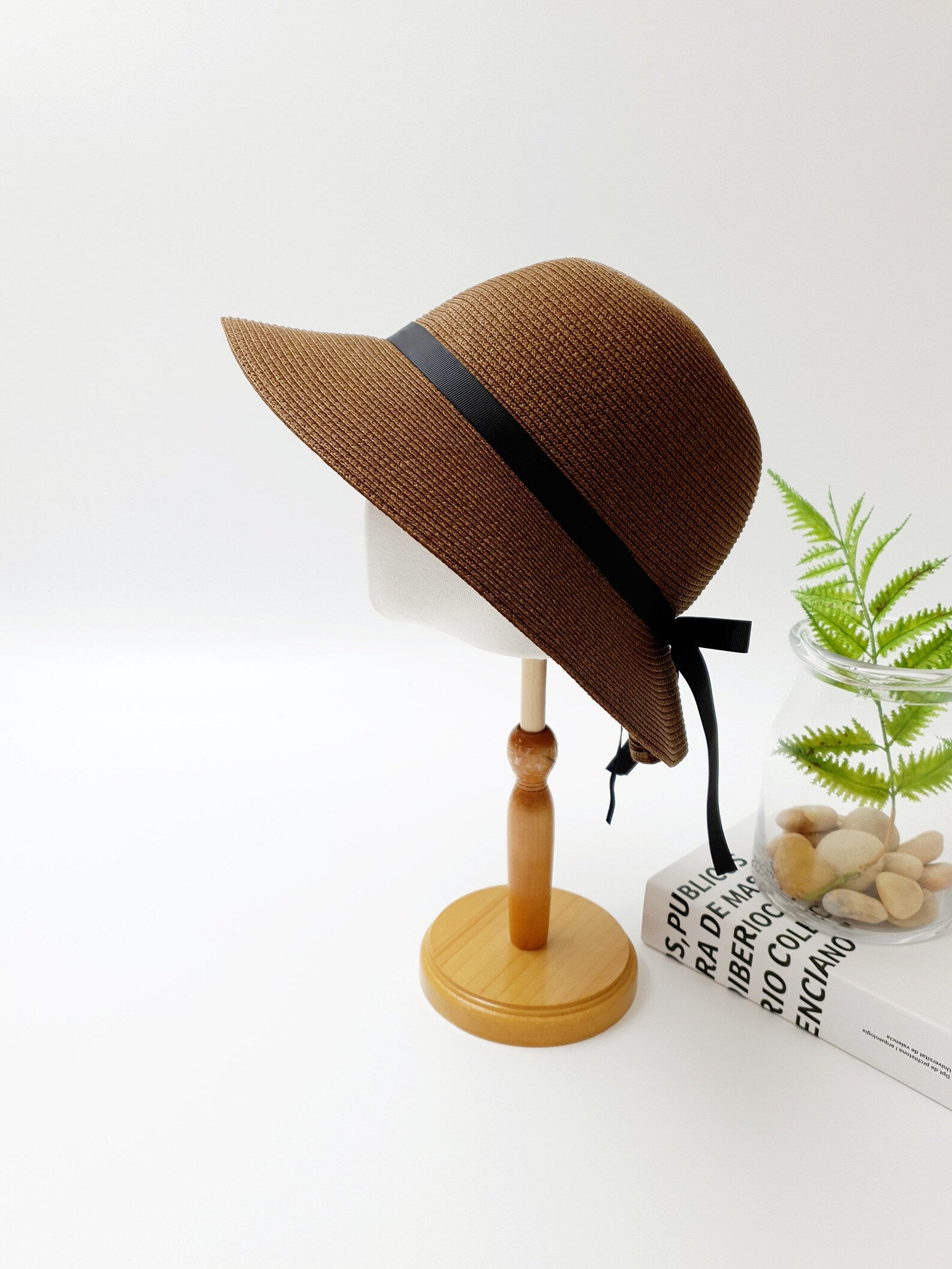 Brown woven julia sun hat with black ribbon detail, displayed on a wooden stand. Classic sun protection with stylish accent.