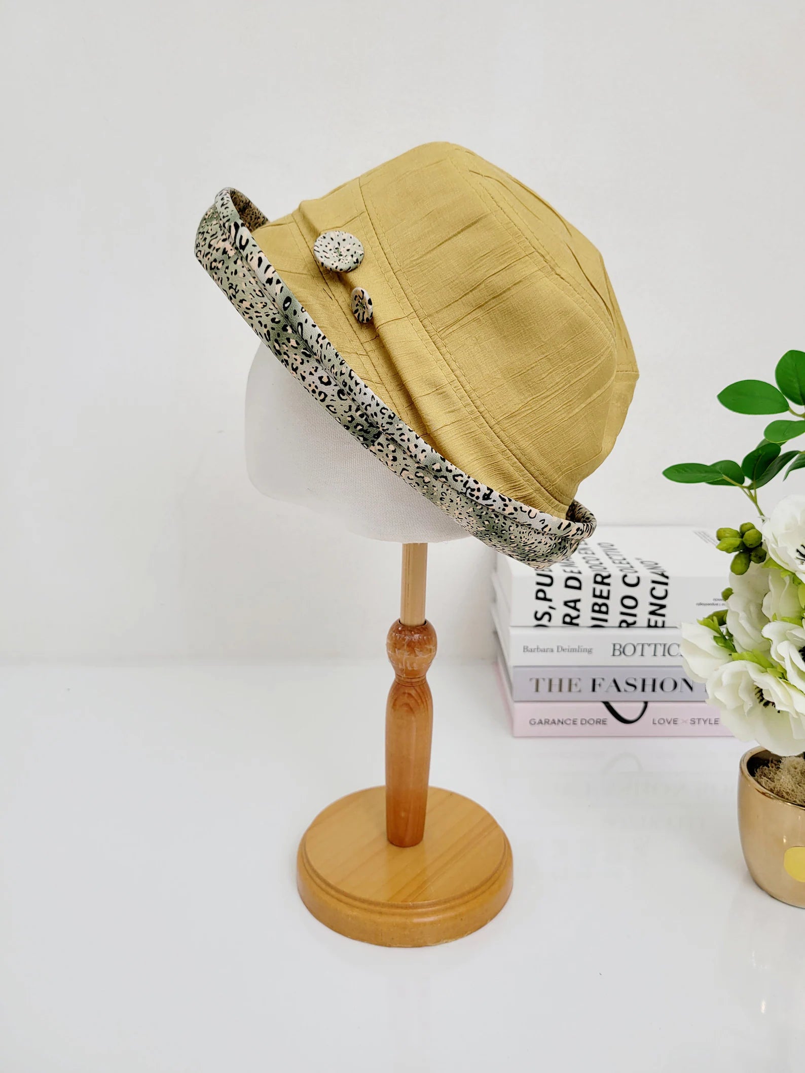 Light yellow leopard linen bucket-folderable hat with patterned brim and button detail on a mannequin head.