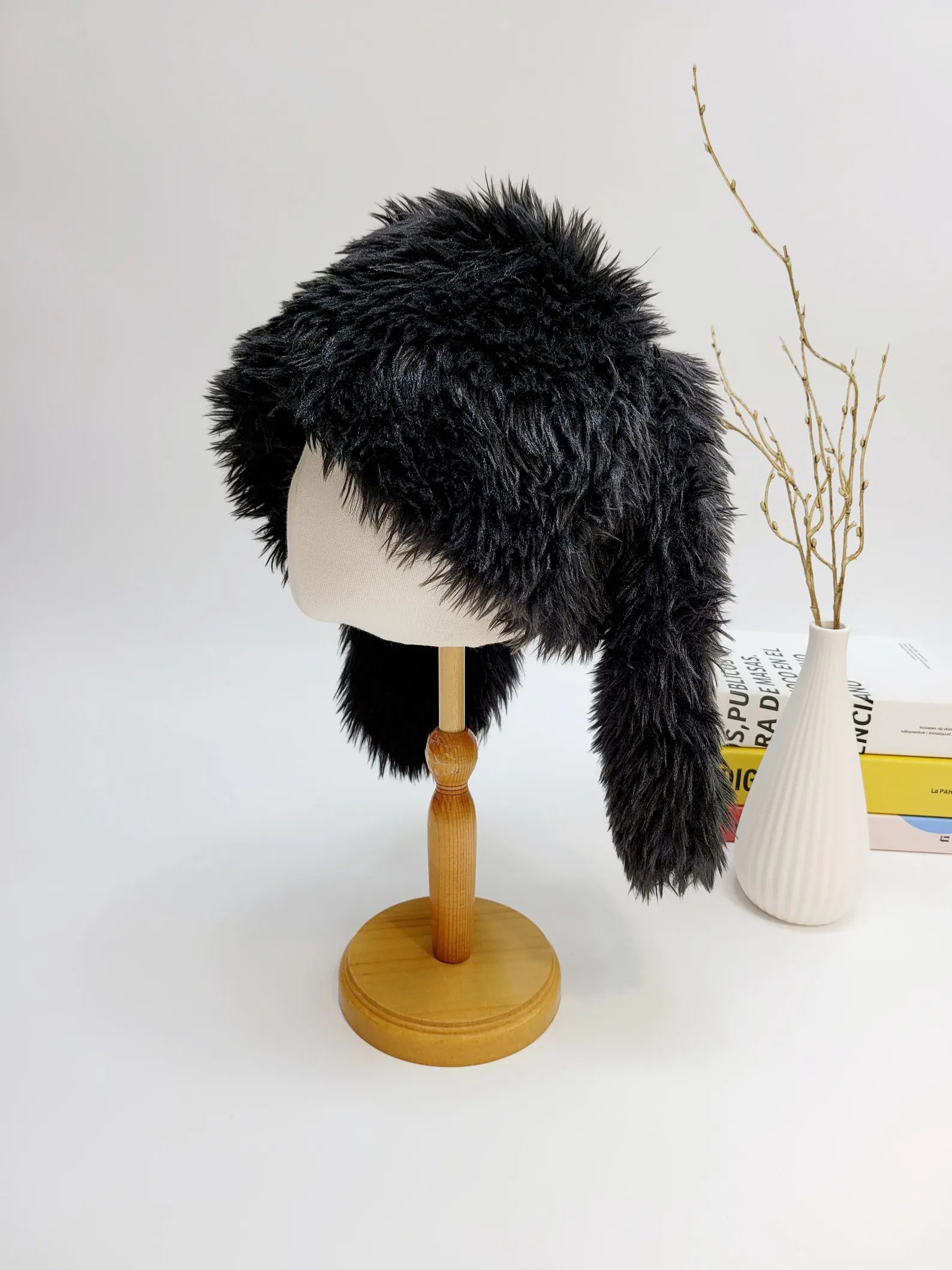 Black faux fur "snow bunny" hat on a mannequin head. The hat has long ear flaps and a fluffy texture.
