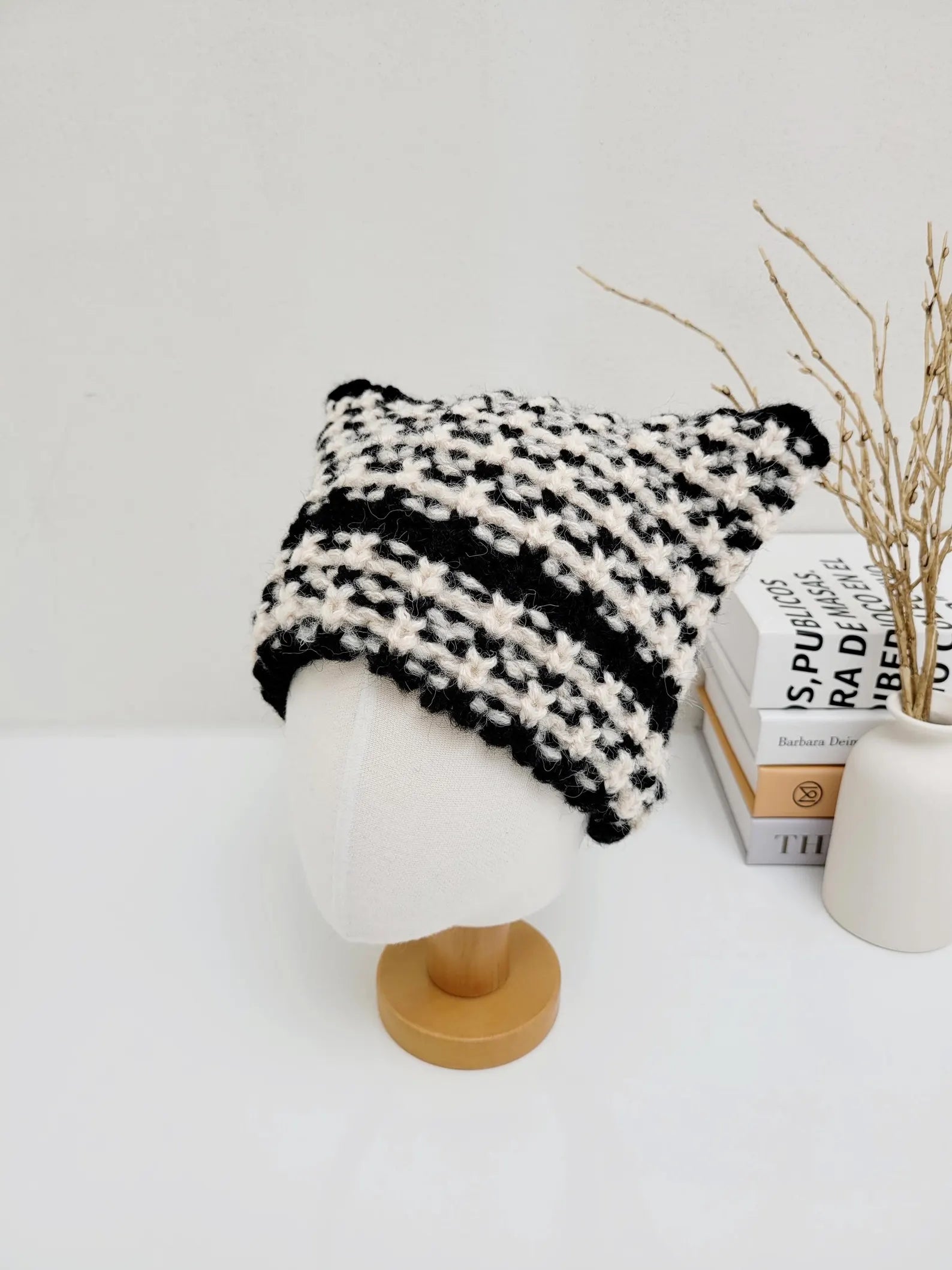 Black and white crocheted cat ear hat on a mannequin head, featuring a textured stitch and playful design.