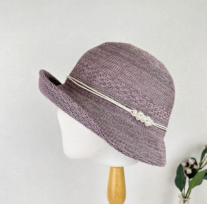 Mauve woven alexandra hat with short brim, adorned with a white cord and pearl details.