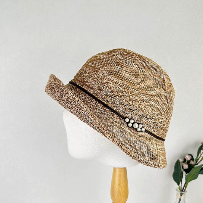 alexandra hat: Brown woven cloche-style hat with a dark band and pearl detail, offering a vintage-inspired look.