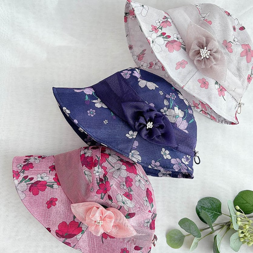 Three queens summer sun hats: pink, navy, and white floral patterns, each with a matching flower detail. Stylish sun protection.