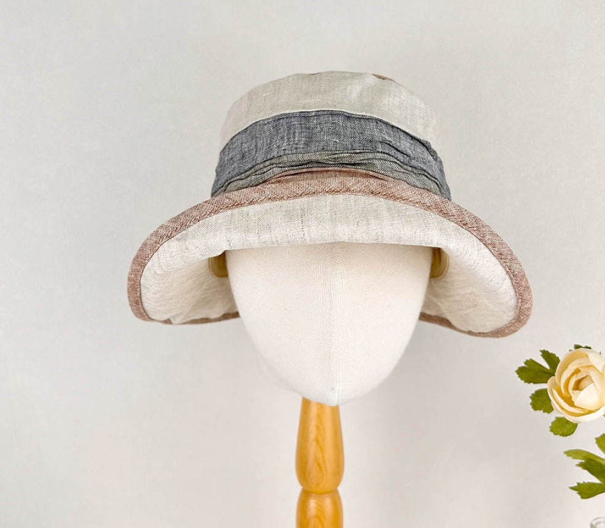 LIC SUMMER BREEZE hat on mannequin. Linen bucket hat in neutral tones with a grey band and brown trim.