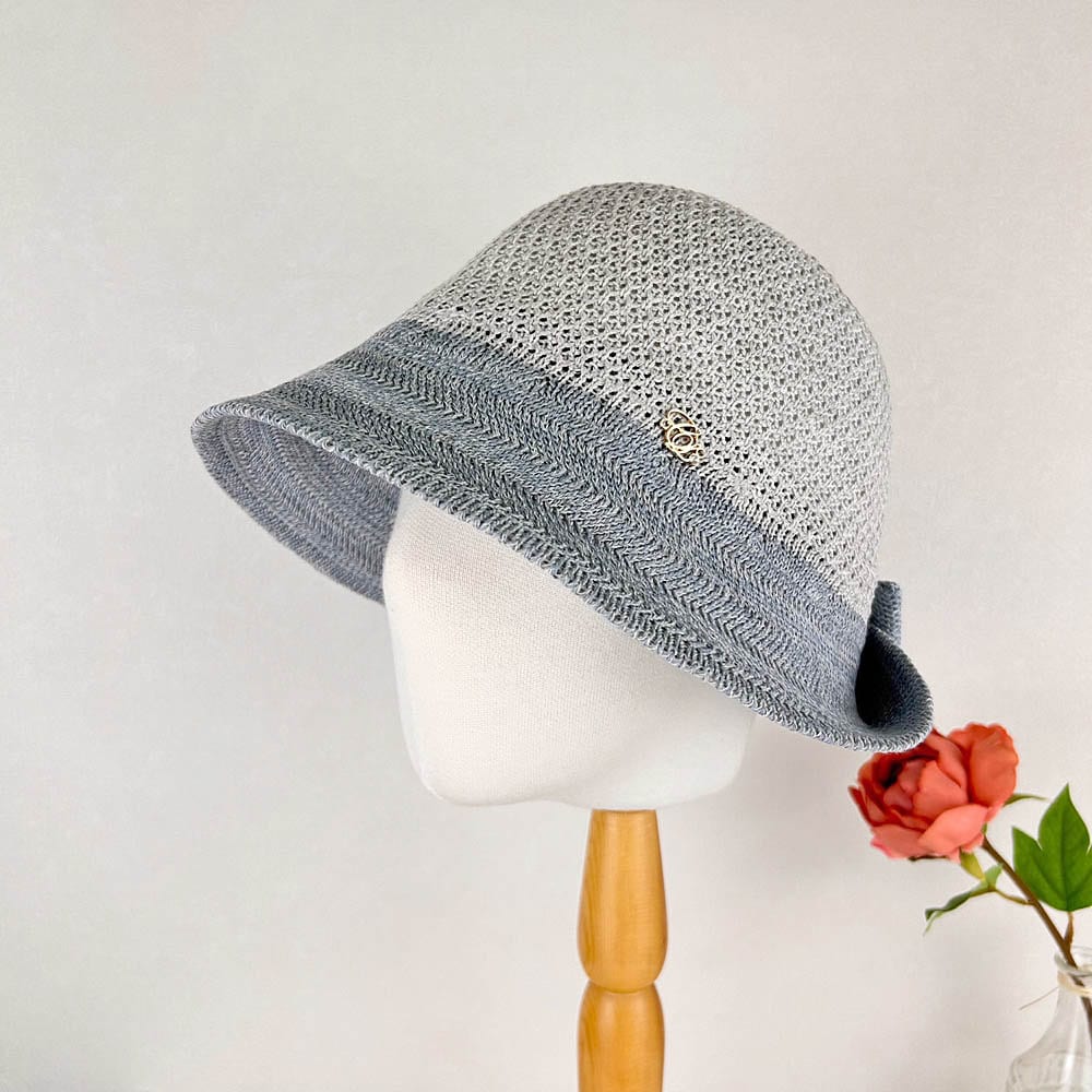Gray and blue knitted victoria's summer hat with a decorative accent, displayed on a mannequin head.