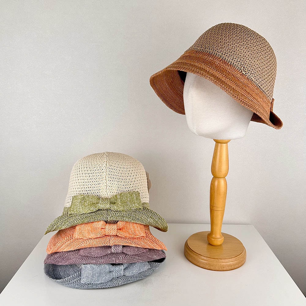 victoria's summer hat: Stacked straw sun hats with decorative bows in green, peach, lavender, and gray, plus a brown hat on a mannequin.