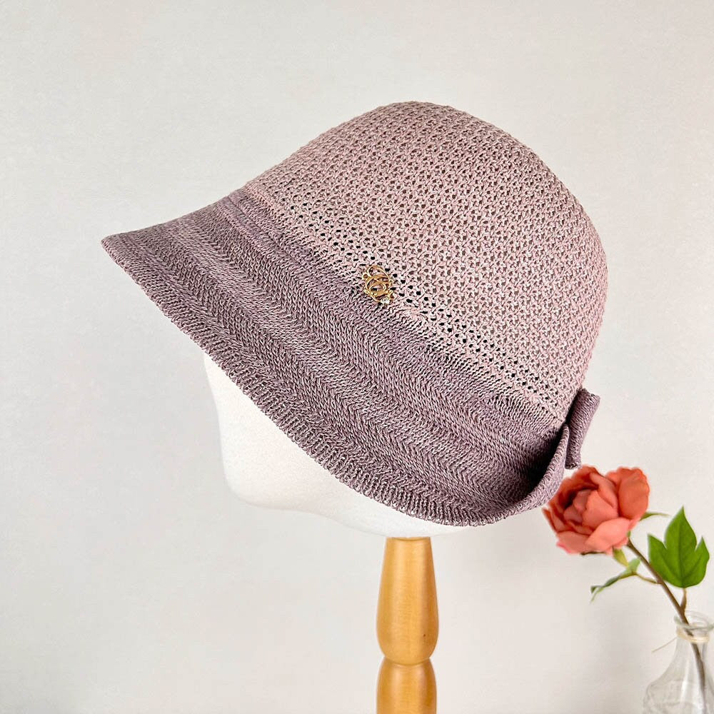 victoria's summer hat: mauve, crocheted hat with a wide brim, decorative side bow, and a small gold-tone embellishment
